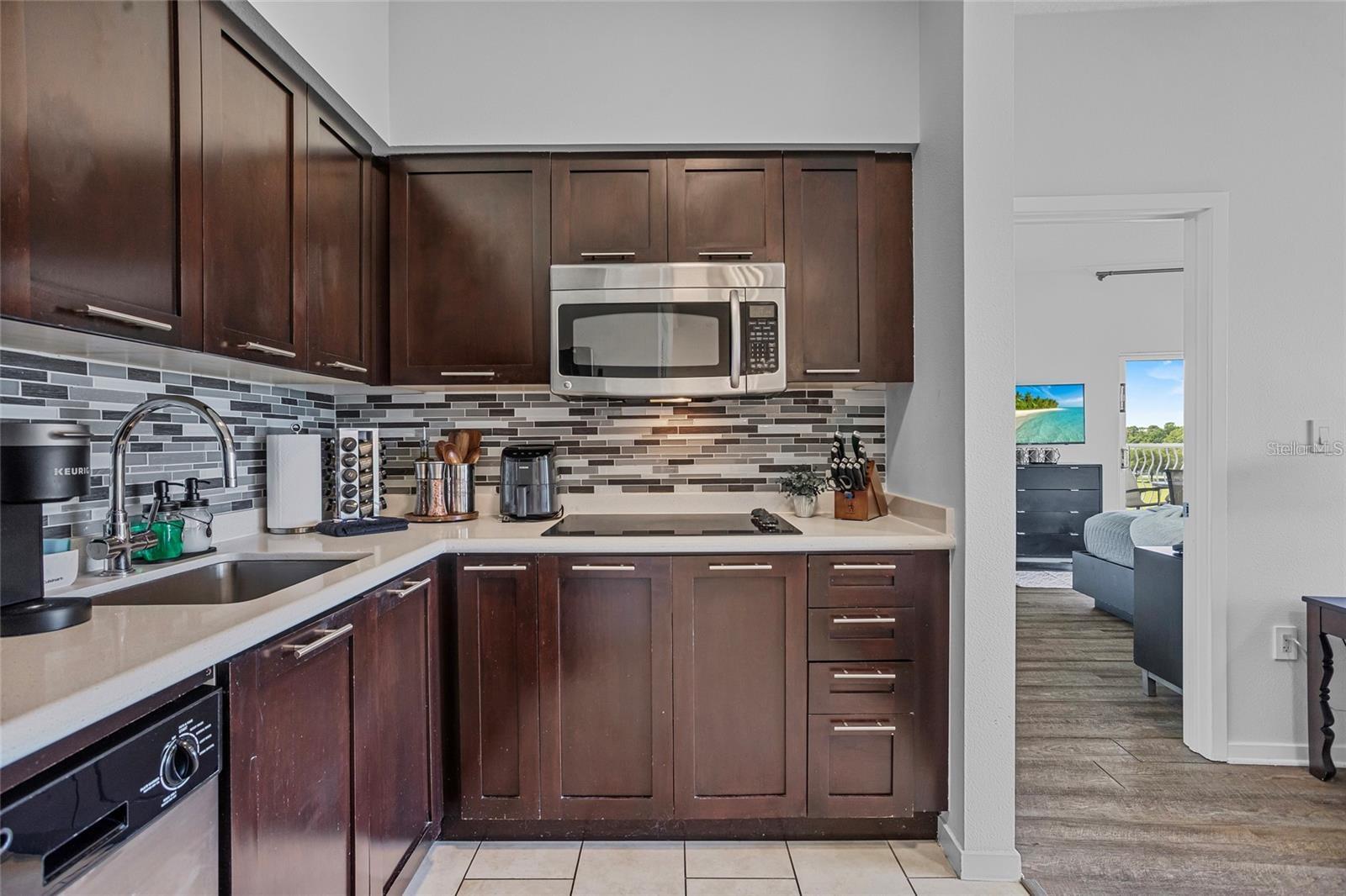 Kitchen with dark wood cabinetry, tile backsplash, and stainless steel appliances, opening to a bedroom and balcony.