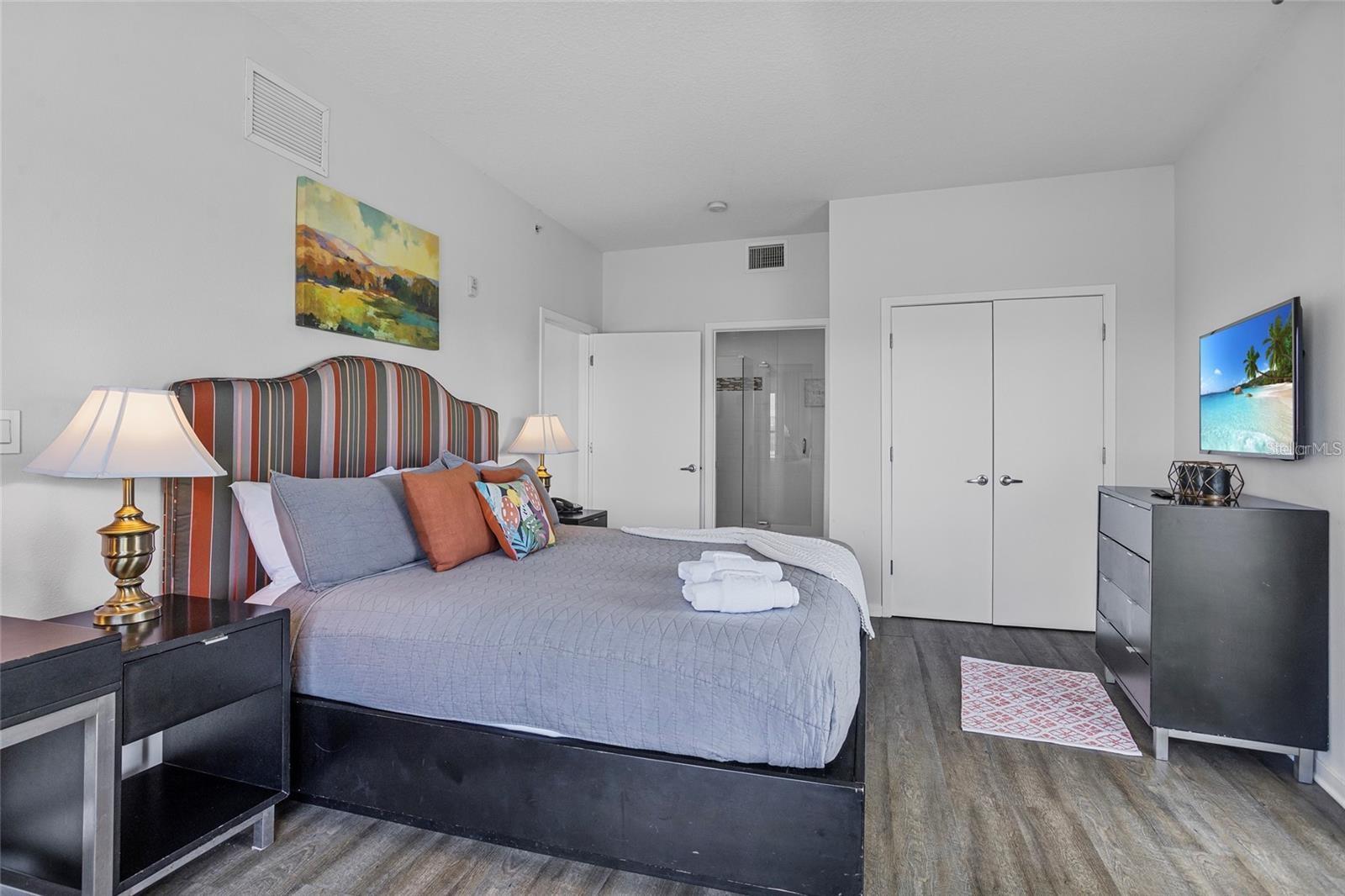 Furnished bedroom with a striped headboard, gray bedding, and a wall-mounted television.