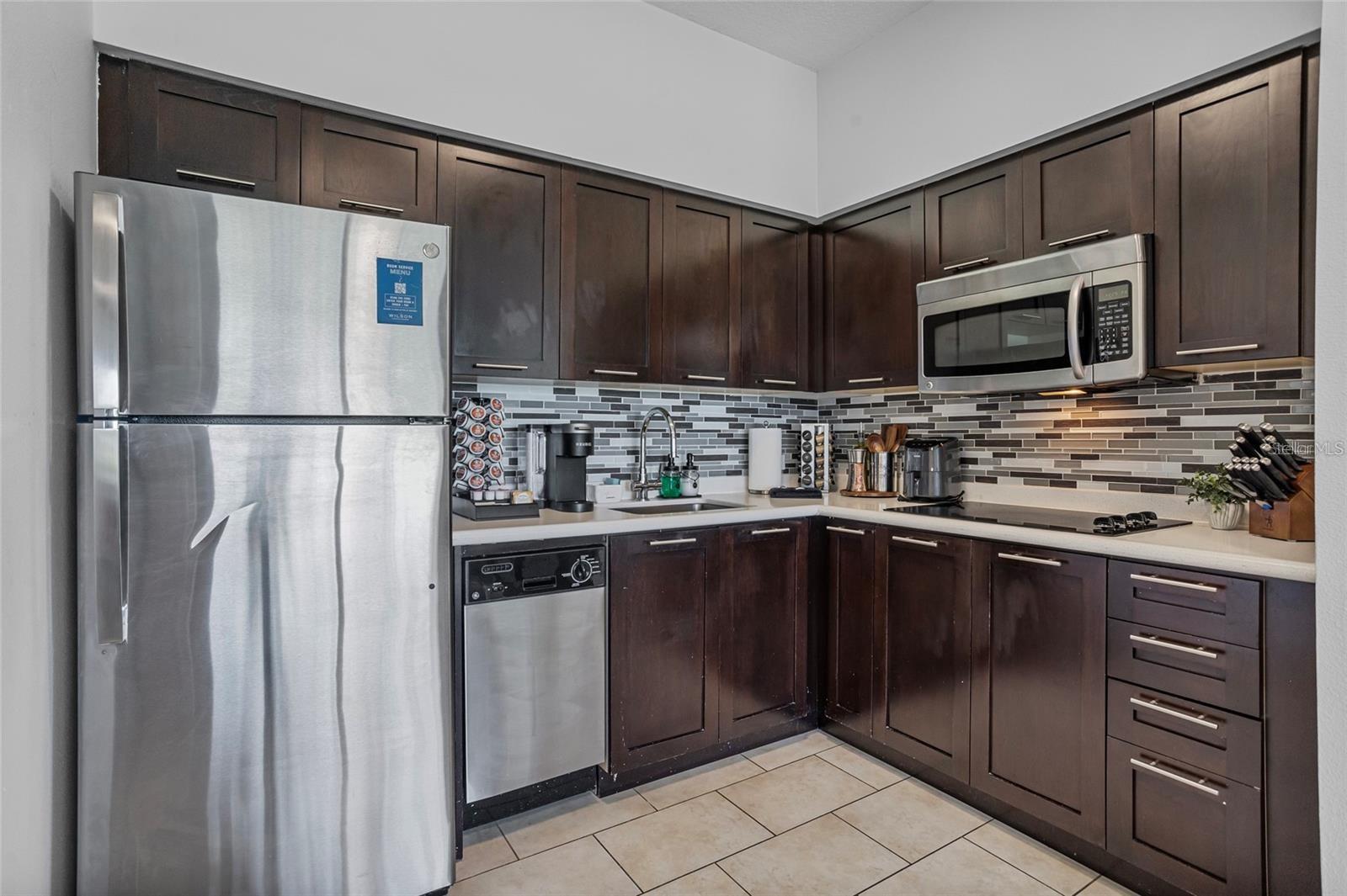 Kitchen with dark wood cabinets, stainless steel appliances and a gray-and-white mosaic tile backsplash.