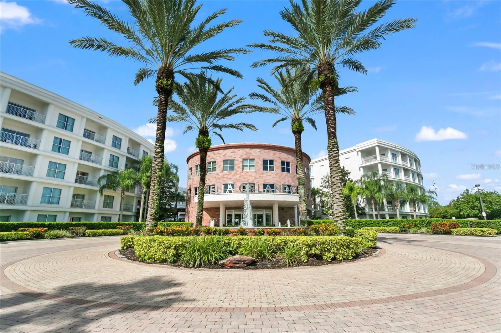 Condominium entrance with a central fountain, tall palm trees, and circular brick-paved drive.
