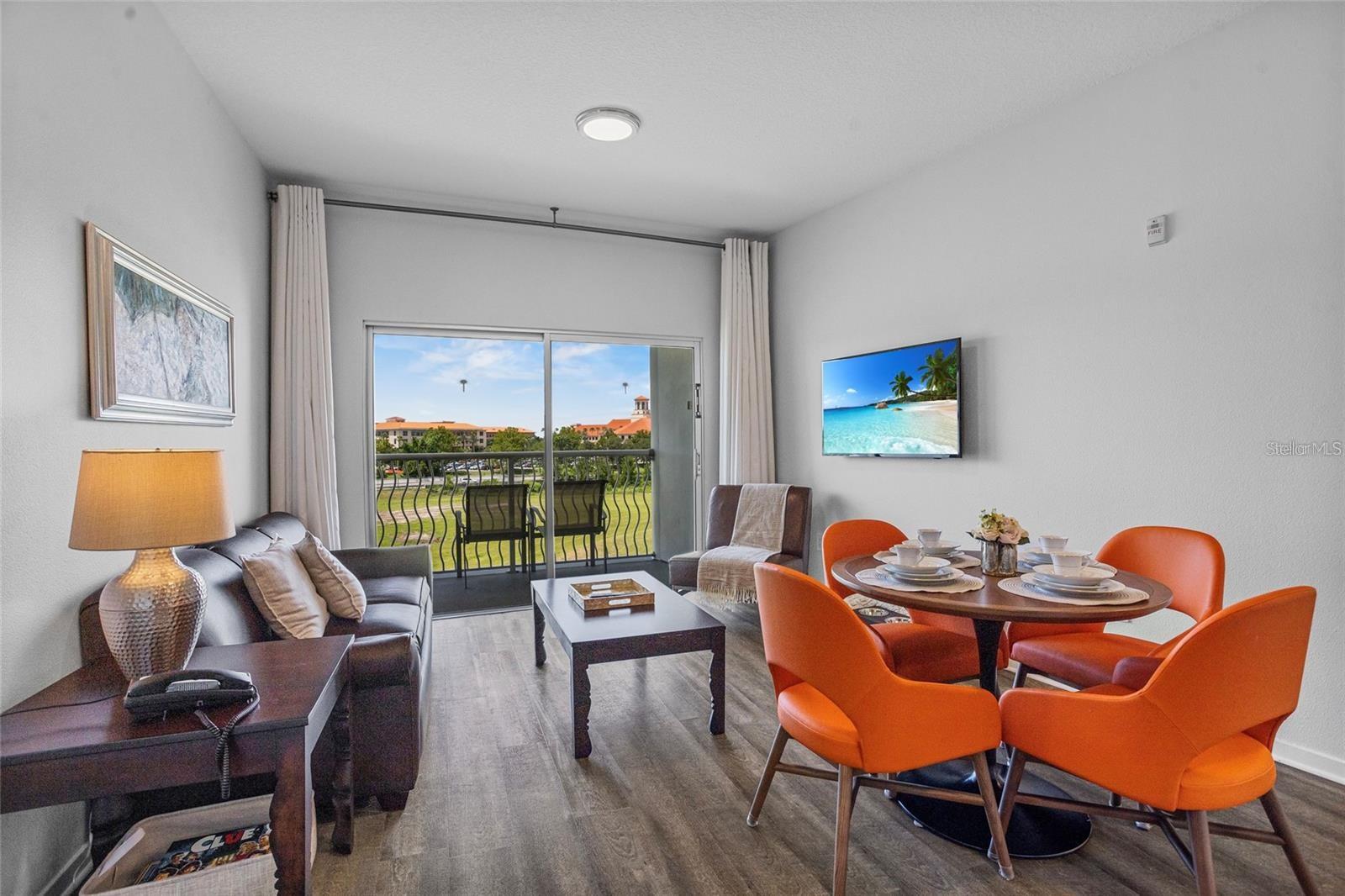 Furnished living and dining room with orange chairs and sliding doors to a balcony.