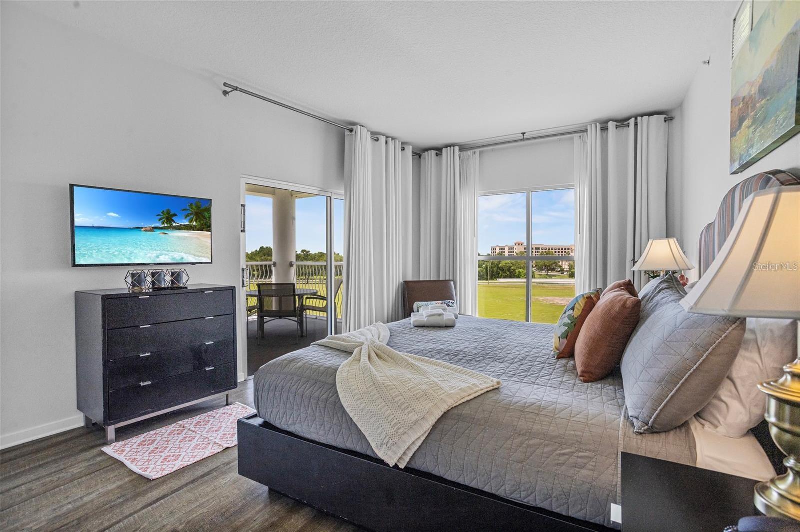 Furnished bedroom with a gray quilted bed and sliding doors overlooking a green lawn.