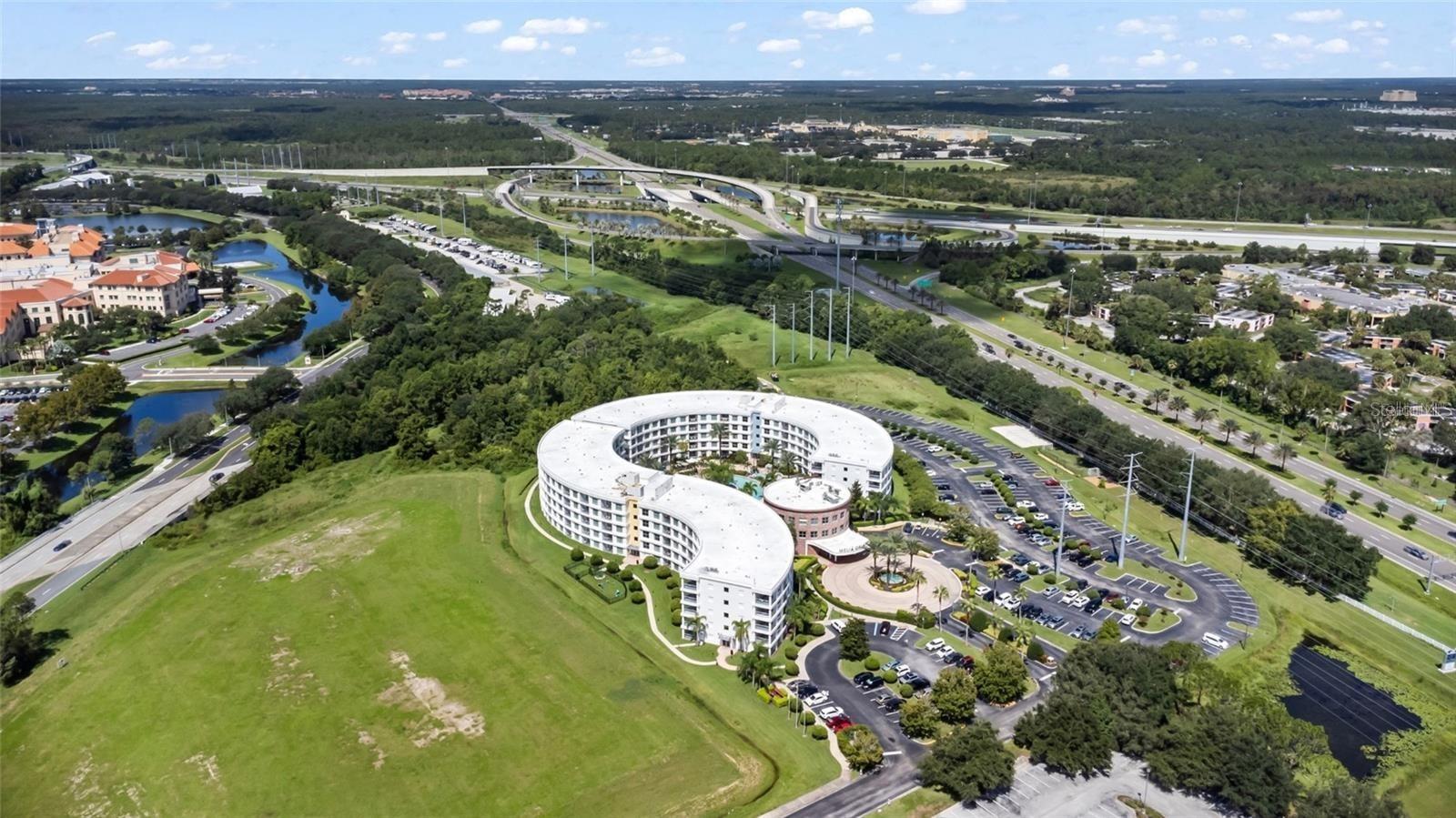 Aerial view of a curved white condominium building with a central courtyard and nearby highway interchange.