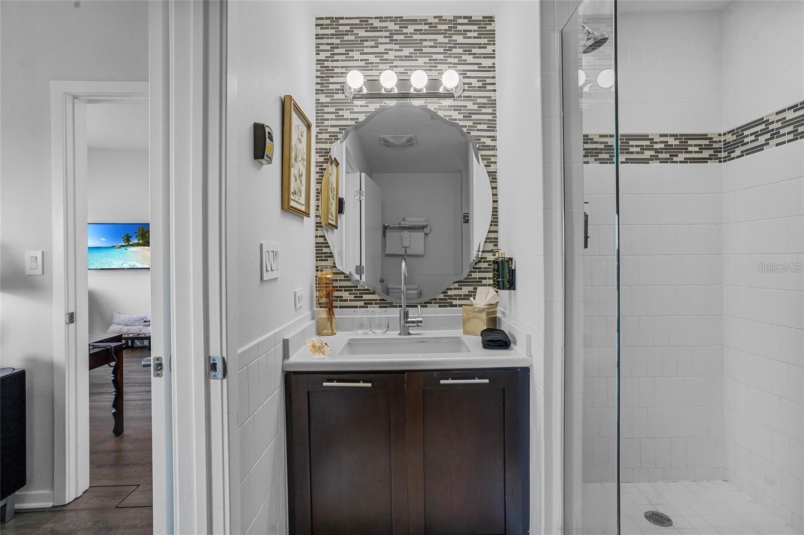 Bathroom with a dark vanity, mosaic tile accent wall, oval mirror, and glass-enclosed shower.