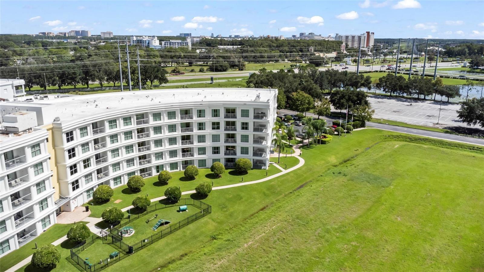 White curved condominium building with landscaped grounds and a distant city skyline.