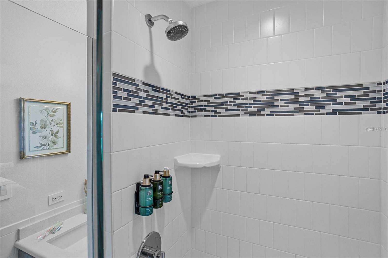 Bathroom shower with a blue and gray mosaic tile accent band and chrome showerhead.