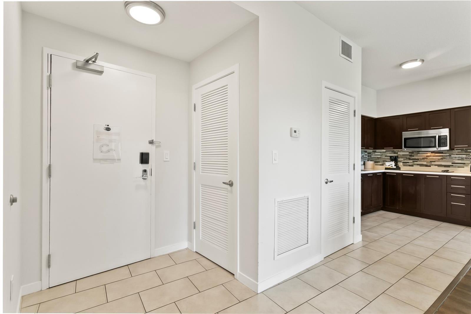 Apartment entryway with beige tile floors and a view into a dark-cabinet kitchen.