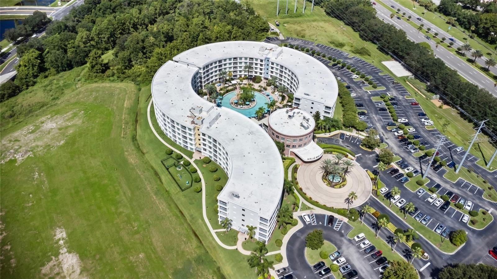 Aerial view of a curved residential building with a central pool and surrounding parking lots.