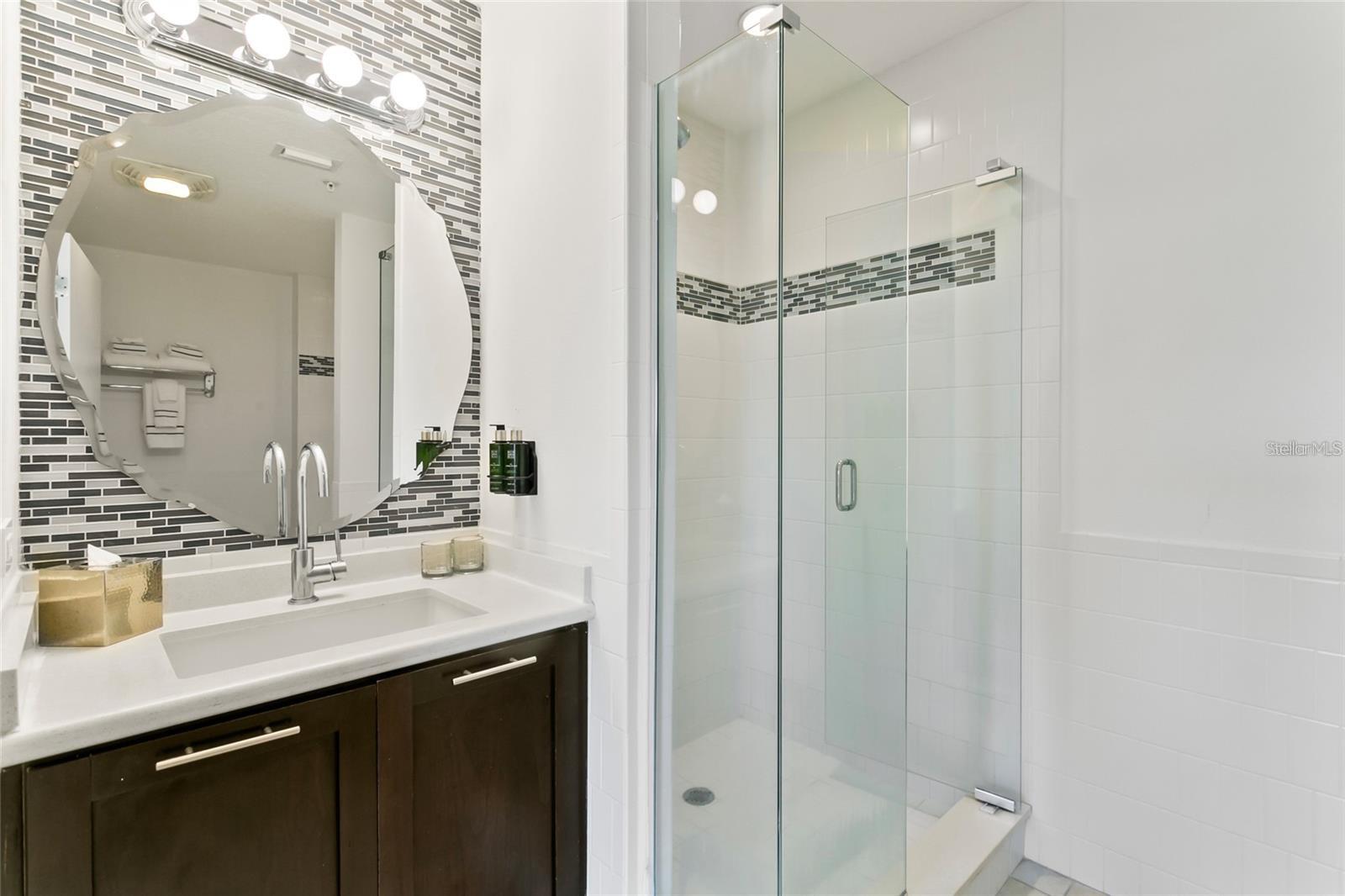 Modern bathroom with a dark wood vanity, mosaic tile accent, and glass-enclosed shower.