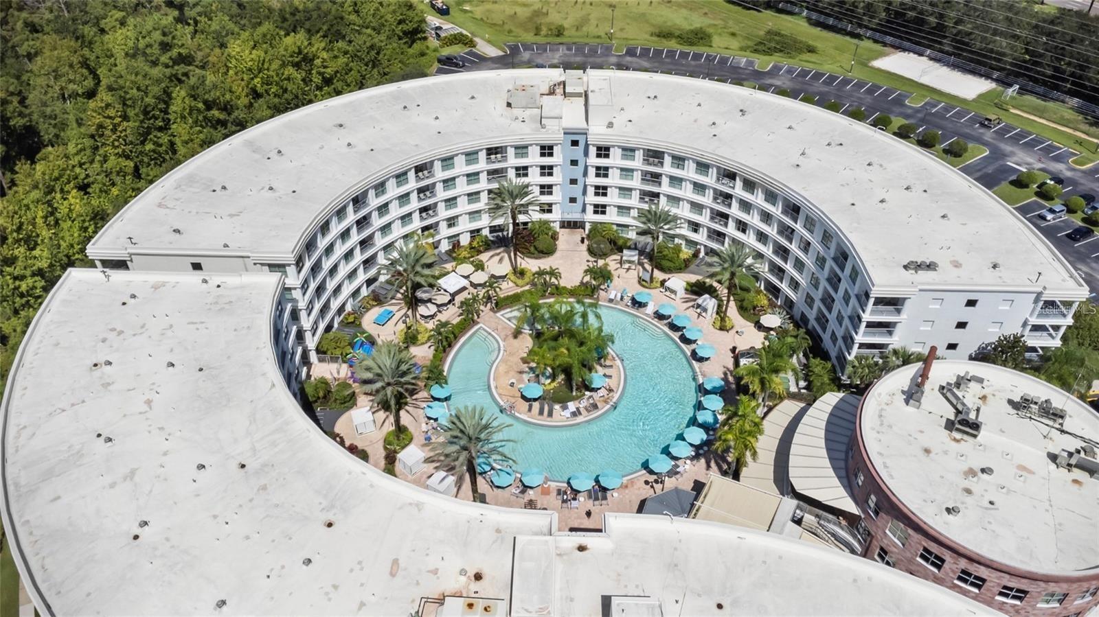 Curved multi-story building enclosing a palm-lined courtyard and winding swimming pool.