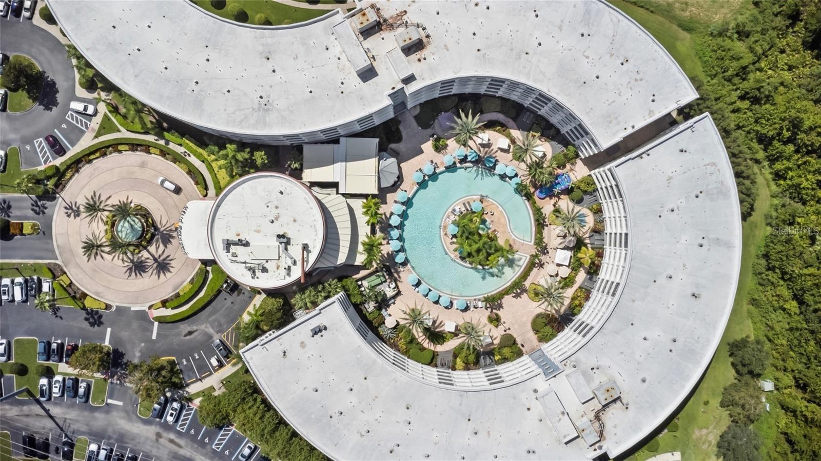 Aerial view of a curved building surrounding a palm-lined courtyard pool.