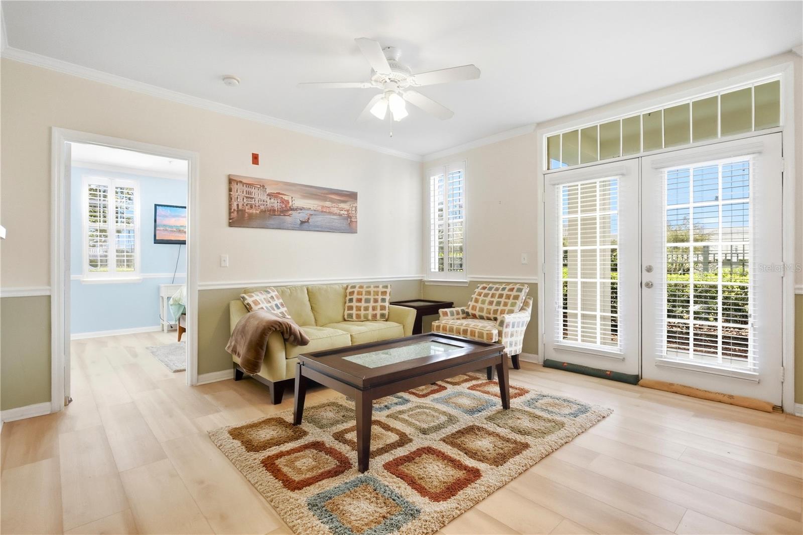 Furnished living room with a cream sofa, patterned armchair, geometric rug, and shuttered glass doors.