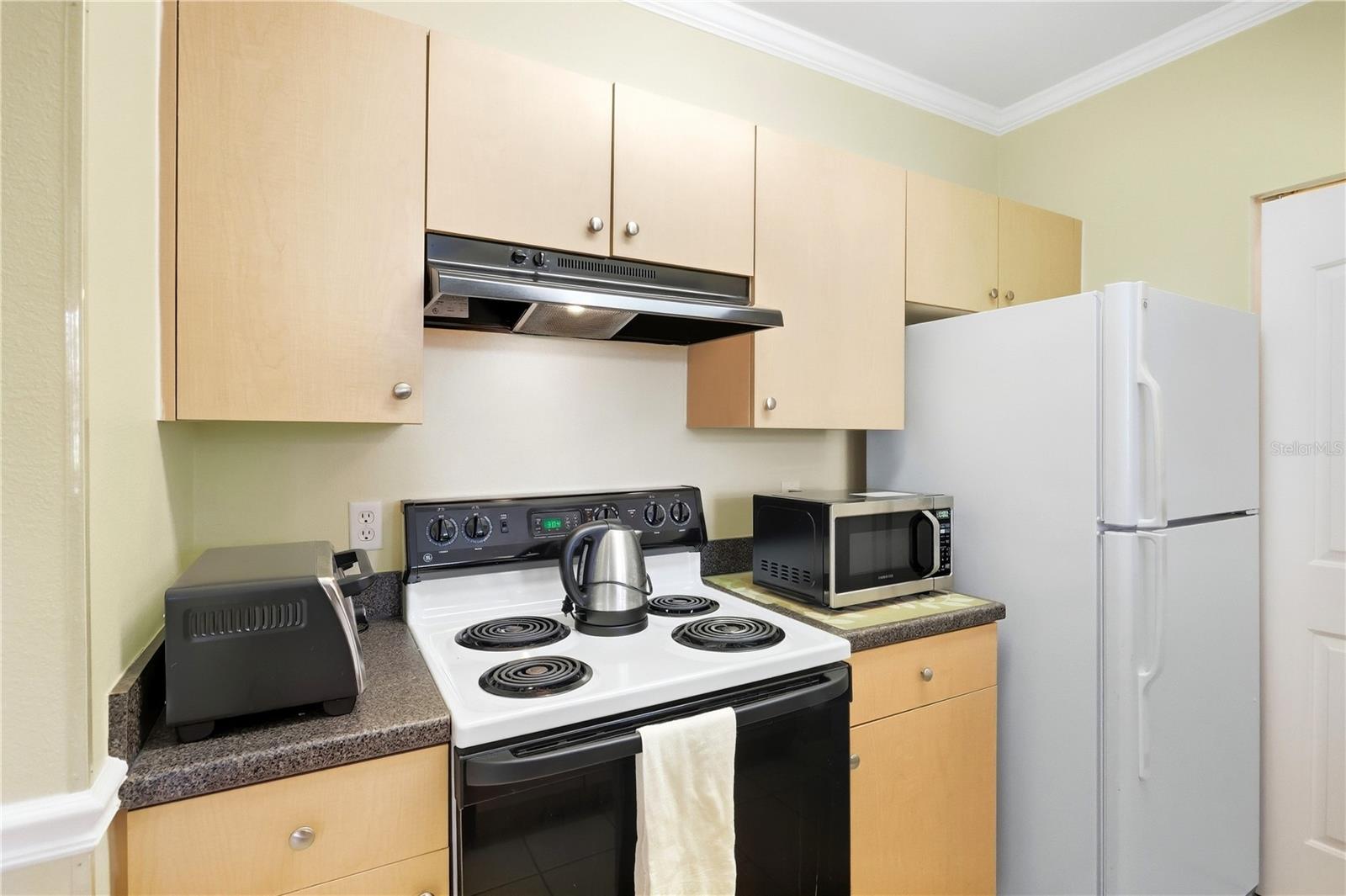 Kitchen with light wood cabinets, electric coil stove, and white refrigerator.