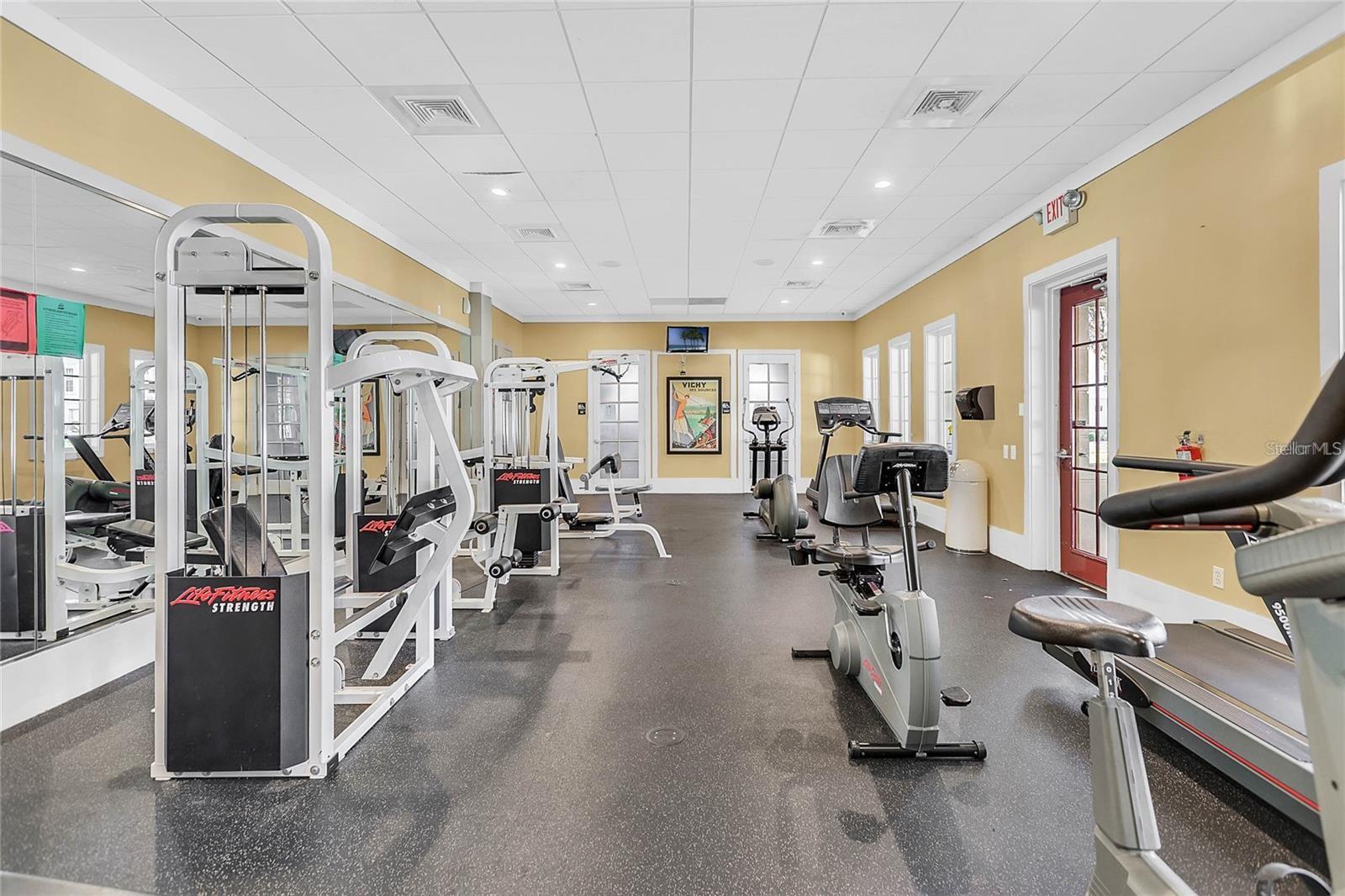 Fitness room with strength machines and cardio equipment beside mirrored walls.