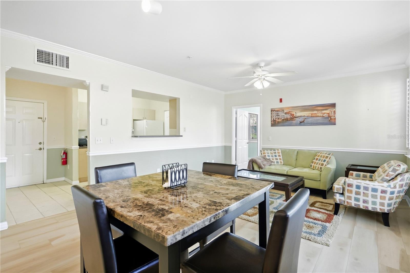 Furnished dining and living area with a stone-pattern table, pale green sofa, and colorful rug.