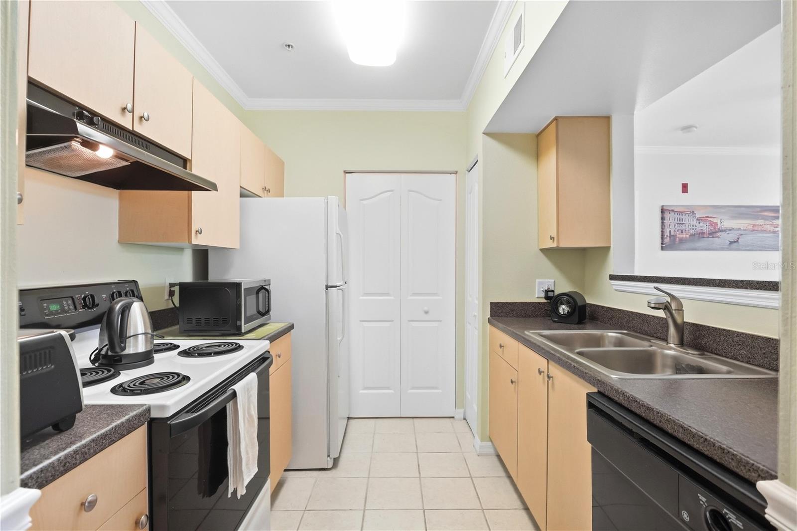 Galley kitchen with light wood cabinets, dark countertops, and a double-basin sink.