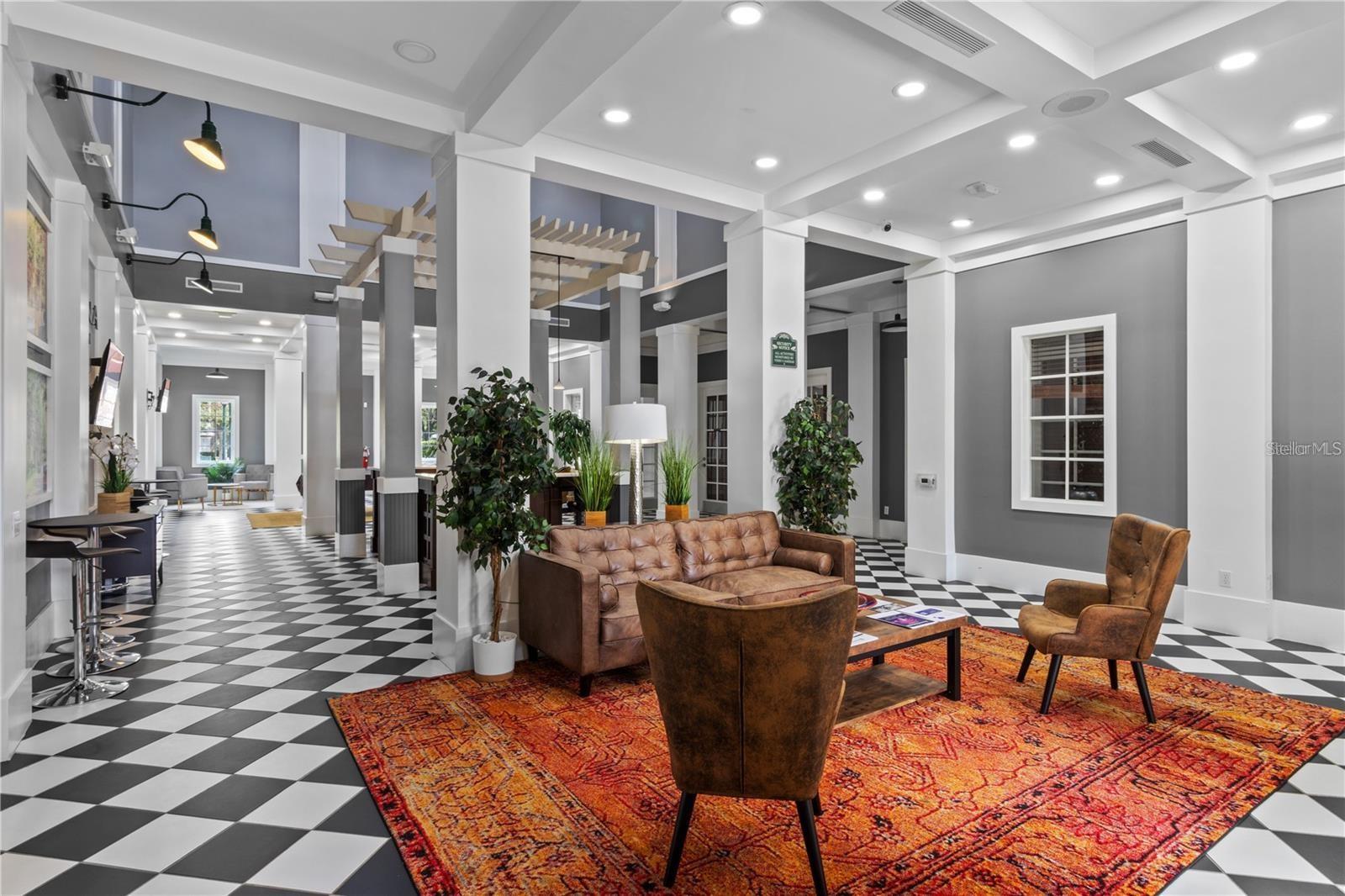 Furnished lobby lounge with leather seating, an orange patterned rug, and black-and-white checkerboard floors.