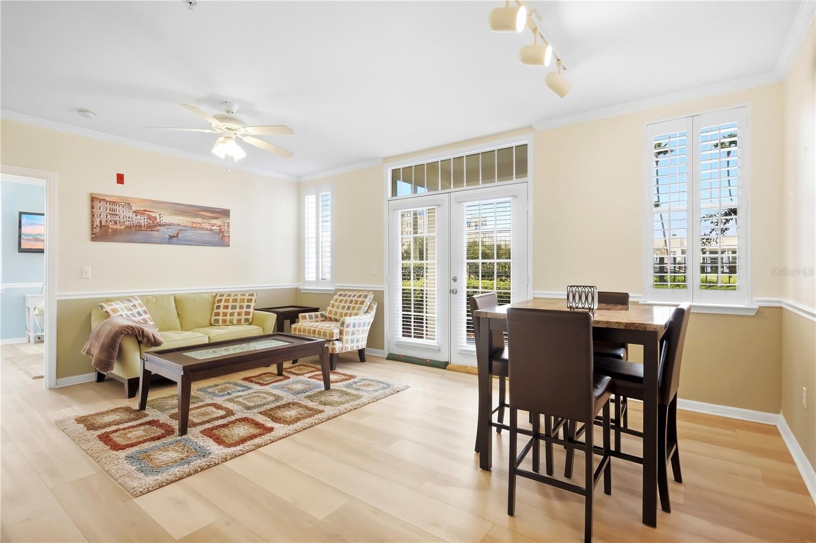 Living and dining room with a yellow sofa, patterned rug, dark dining set, and shuttered windows.