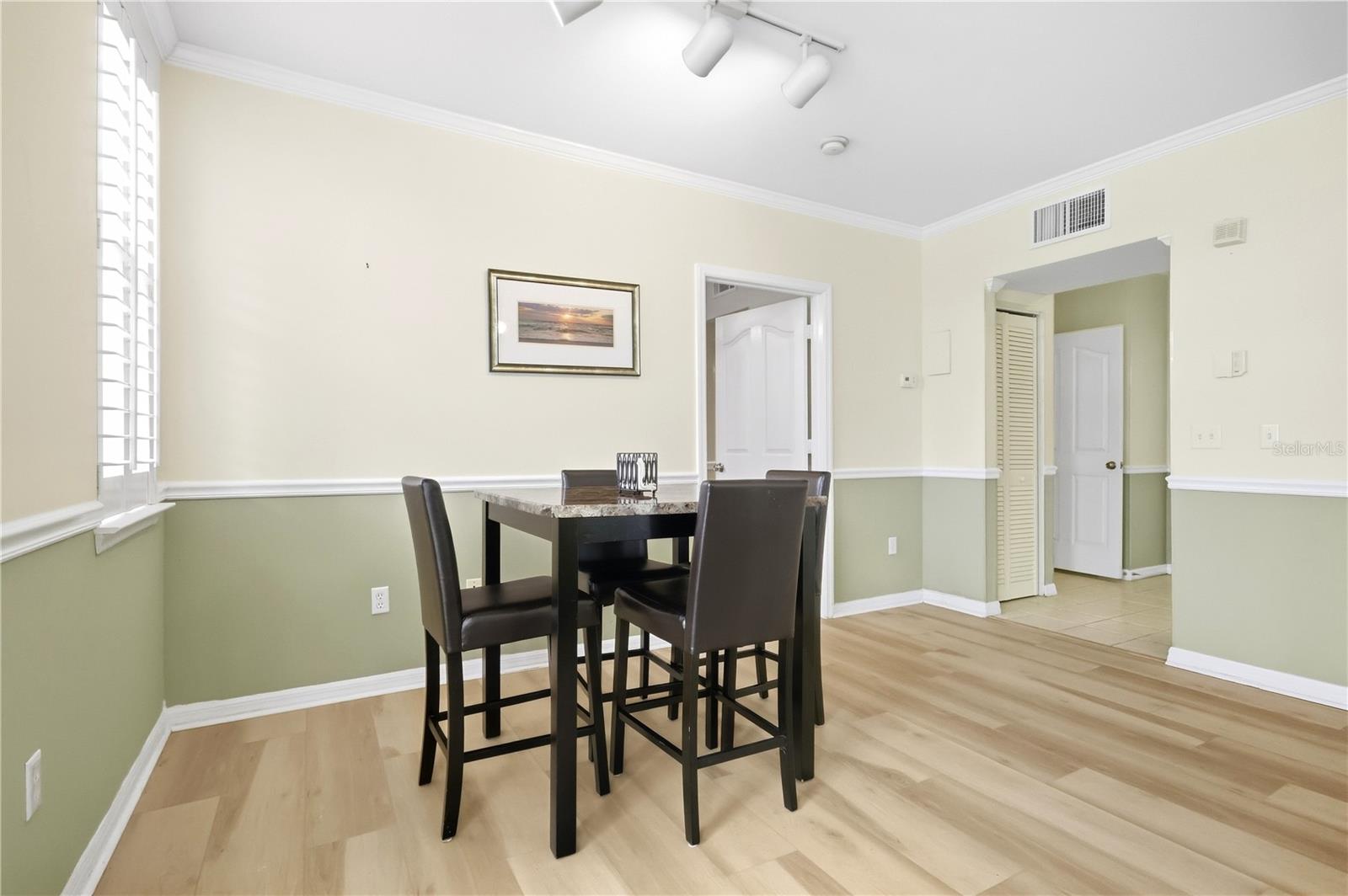 Dining area with a dark table and chairs, two-tone walls, and light wood flooring.