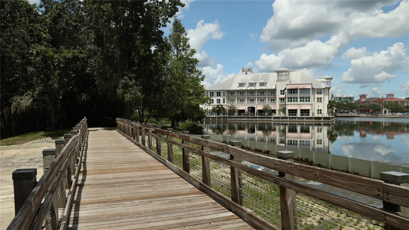 Waterfront community building reflected in a lake, viewed from a wooden boardwalk.
