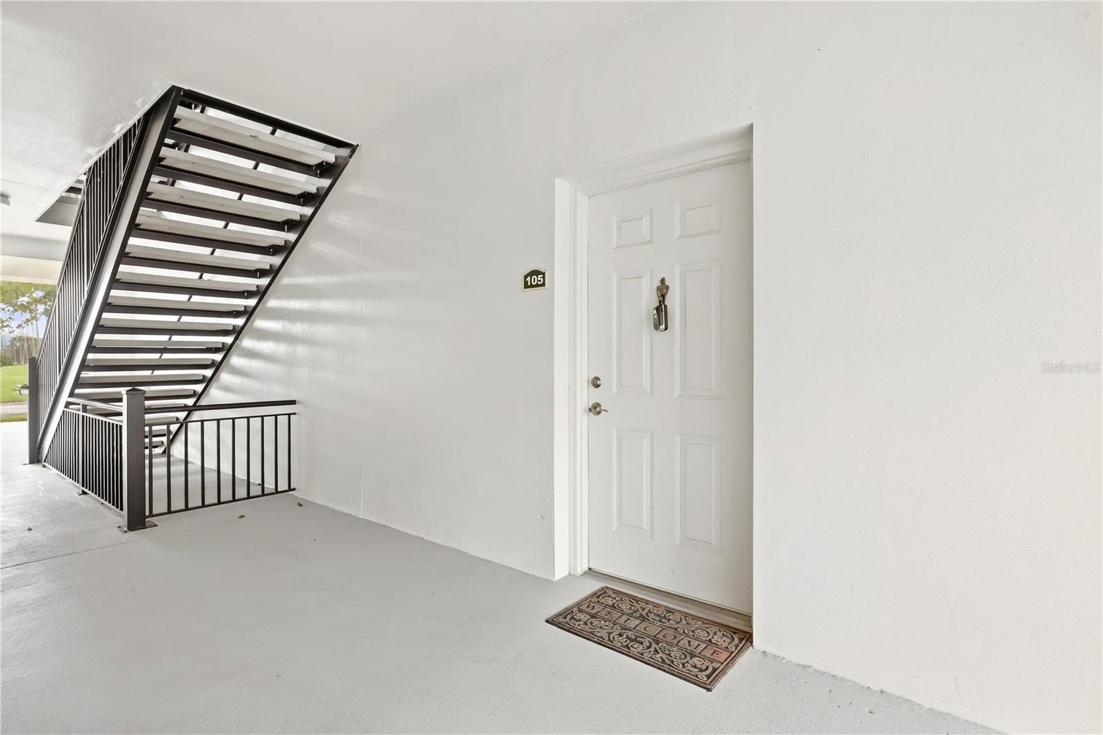 Unit 105 exterior entrance with a white door beside a black metal staircase.