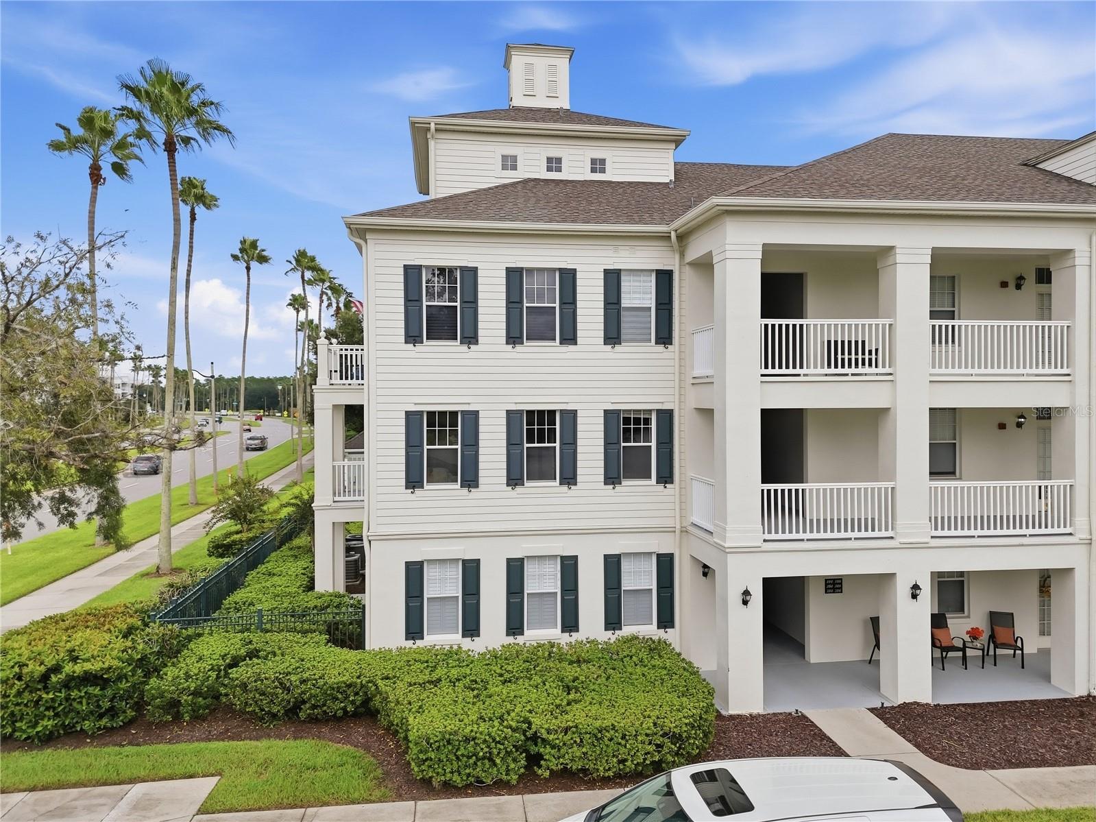 Multi-story residential building with covered balconies, dark shutters, and landscaped grounds.