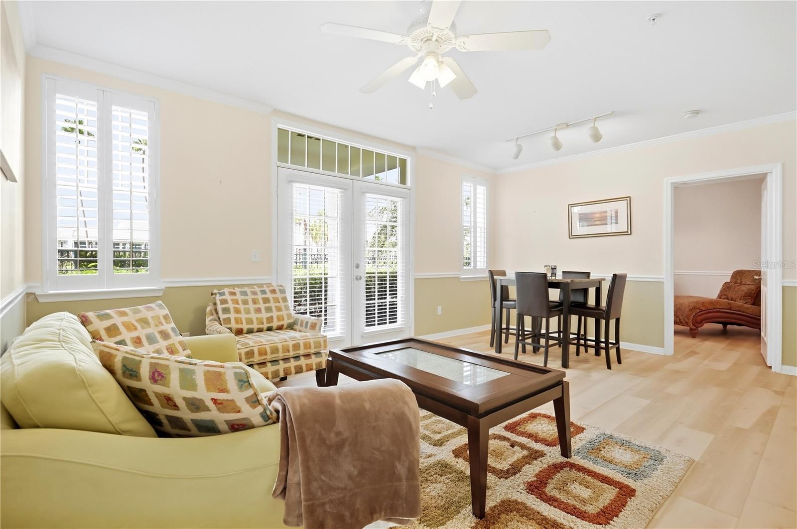 Bright living and dining area with plantation shutters, French doors, and pale wood floors.