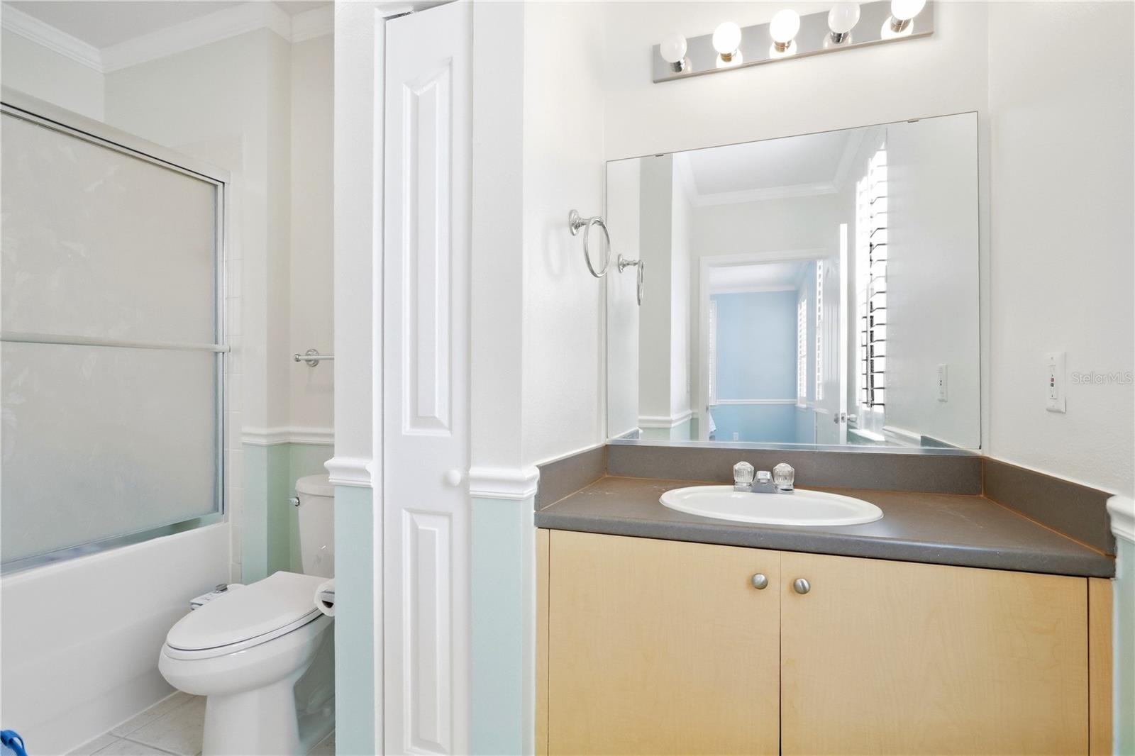 Bathroom with a frosted-glass tub and shower, light wood vanity, and pale mint wainscoting.