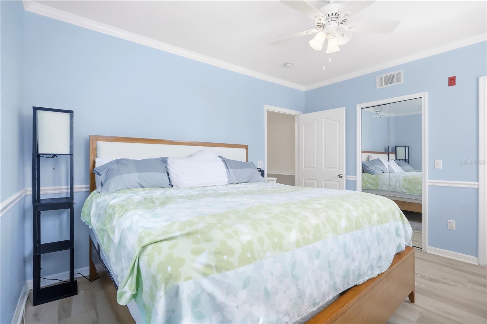 Bedroom with a wood-framed bed, pale green bedding, mirrored closet doors, and blue walls.