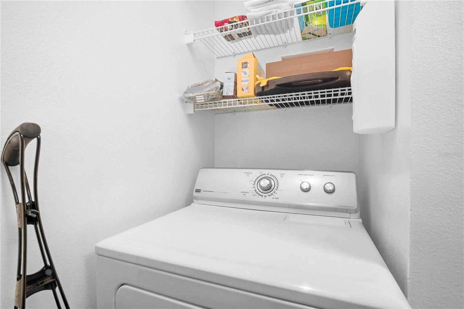 Laundry closet with a top-loading dryer, wire shelves, and an ironing board.