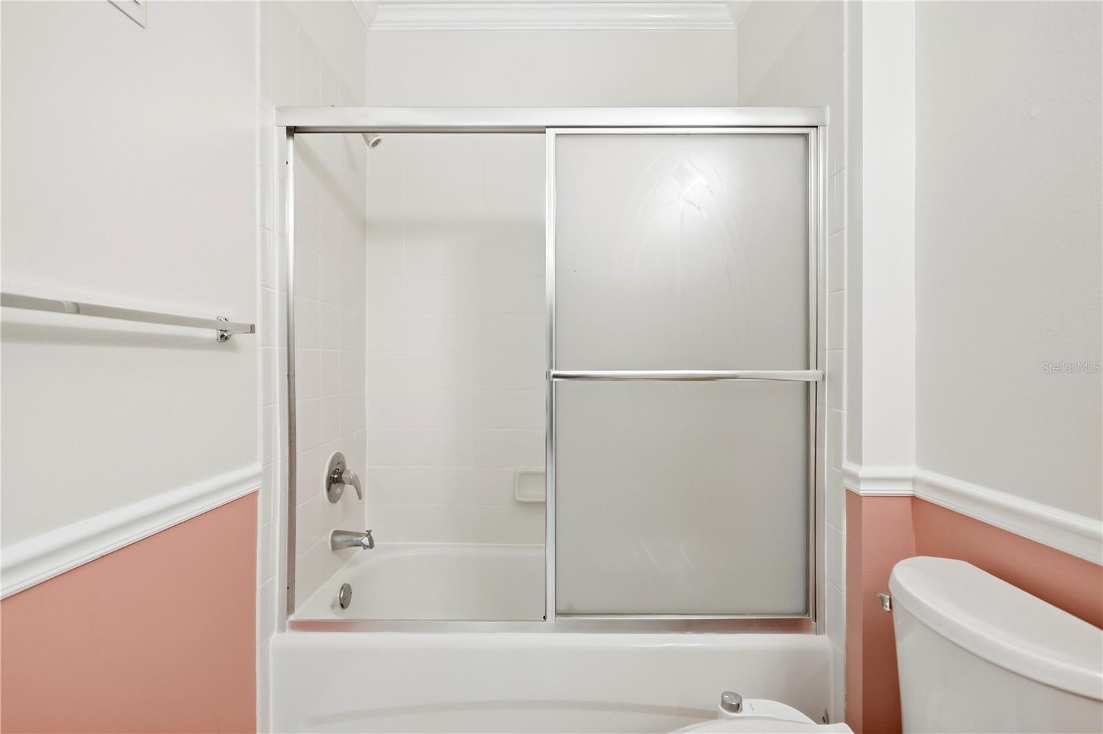 Bathroom with a bathtub and sliding frosted-glass shower doors, white tile, and coral-pink lower walls.