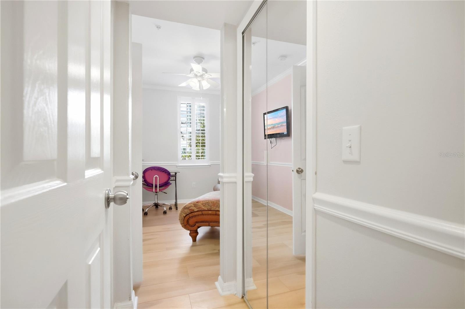 Bedroom with mirrored closet doors, pale wood floors, and a purple desk chair by a shuttered window.