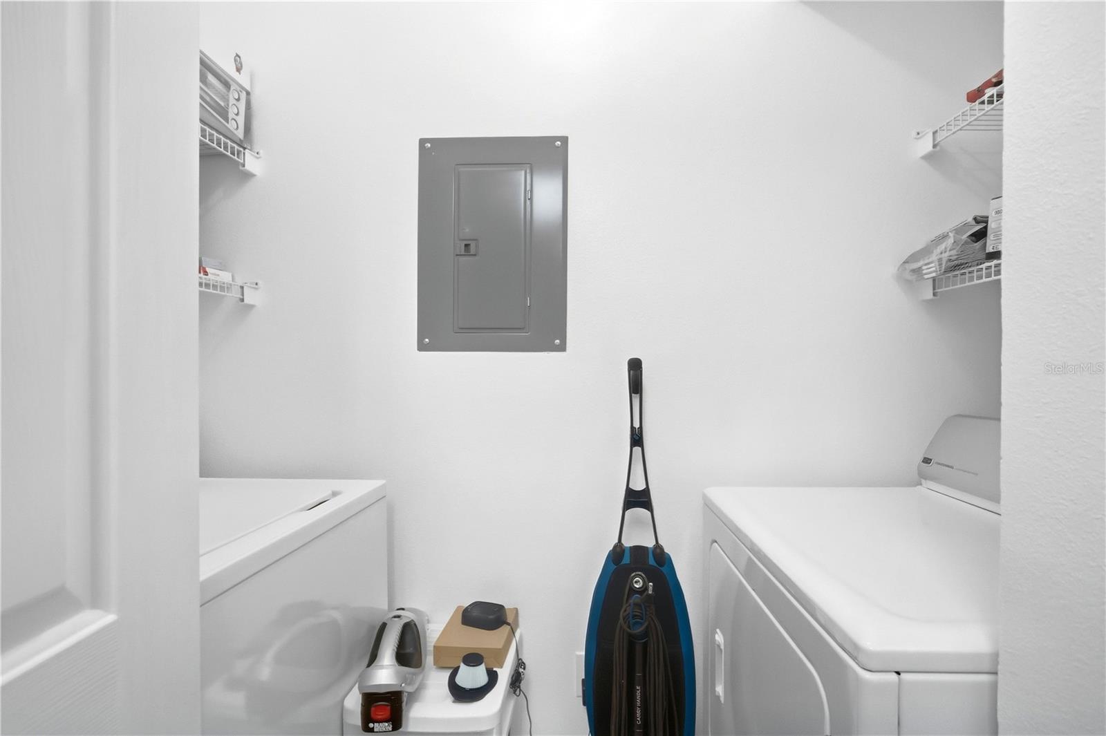 Laundry room with washer and dryer, wire shelves, and a vacuum.