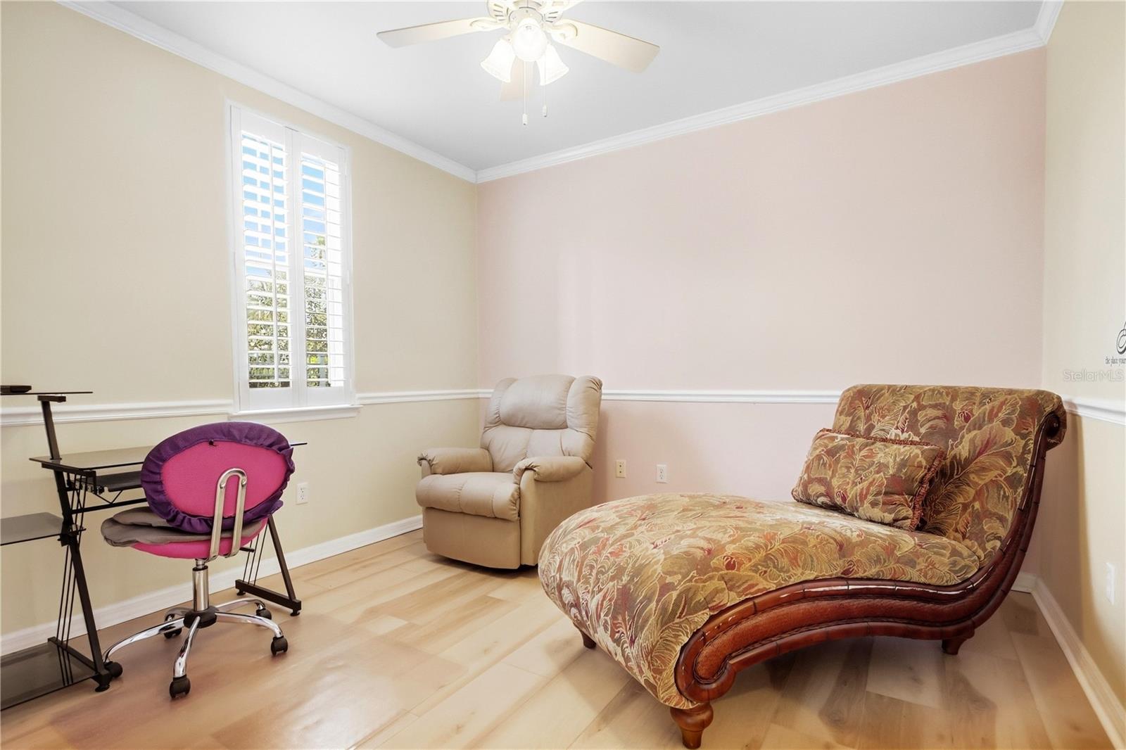 Bedroom with a patterned chaise lounge, beige recliner, and plantation-shuttered window.