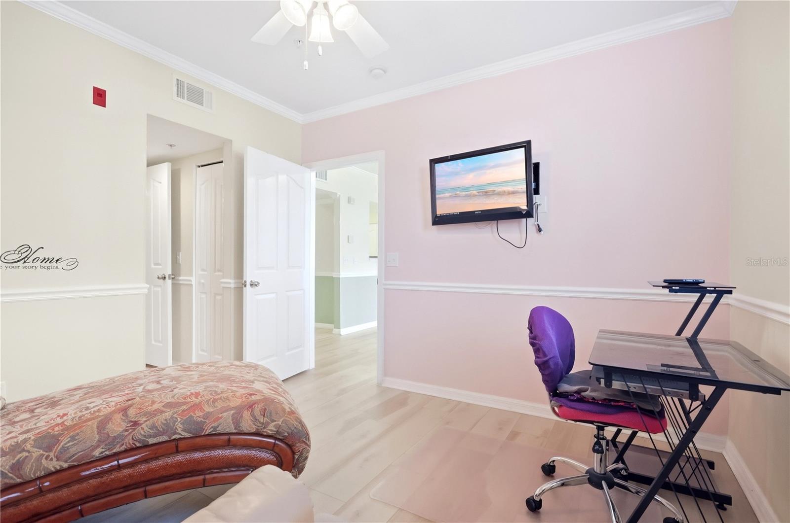 Bedroom with pale pink walls, a wall-mounted television, and a desk with a purple chair.