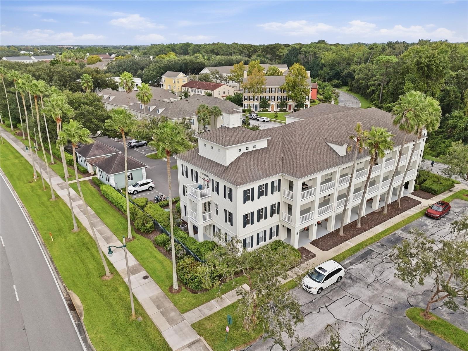 Aerial view of a white multi-story building with covered balconies and palm trees.