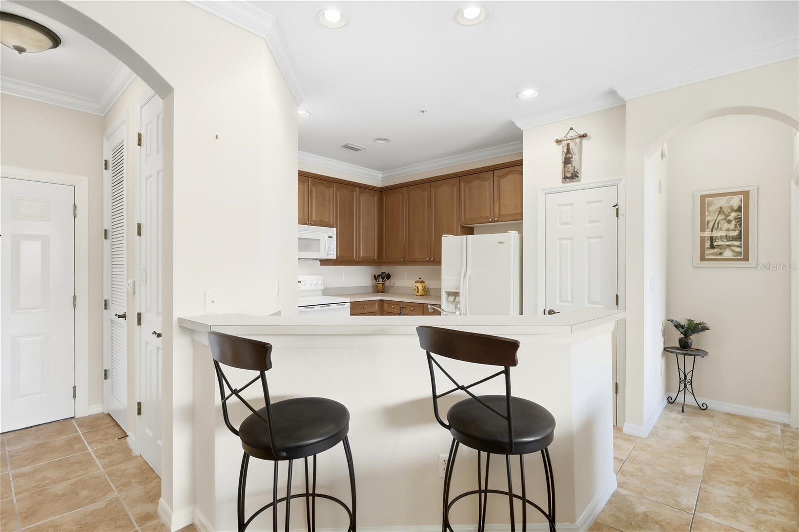 Kitchen with warm wood cabinets, white appliances, and a breakfast bar with two black stools.