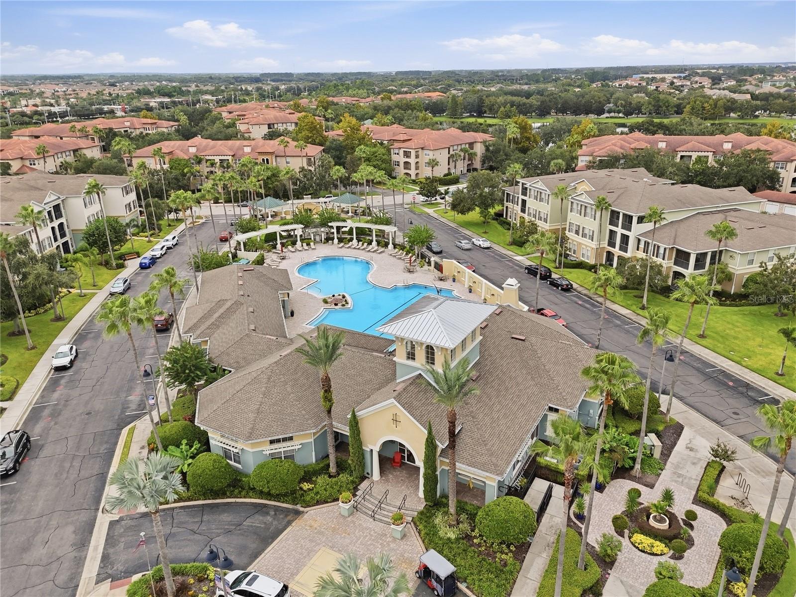 Aerial view of a condominium community with a central swimming pool and palm-lined grounds.