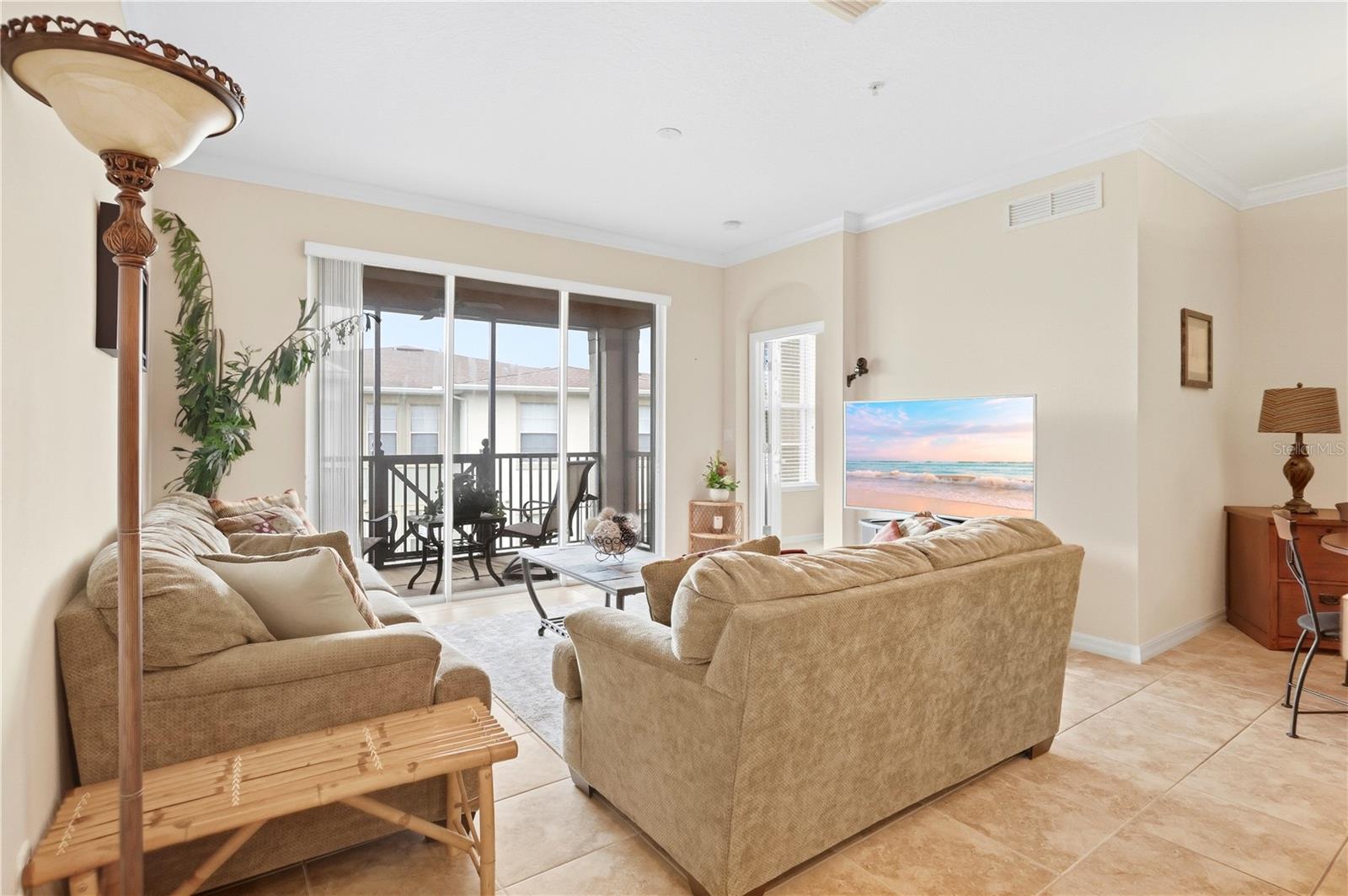 Living room with tan sofas and sliding glass doors opening to a screened balcony.