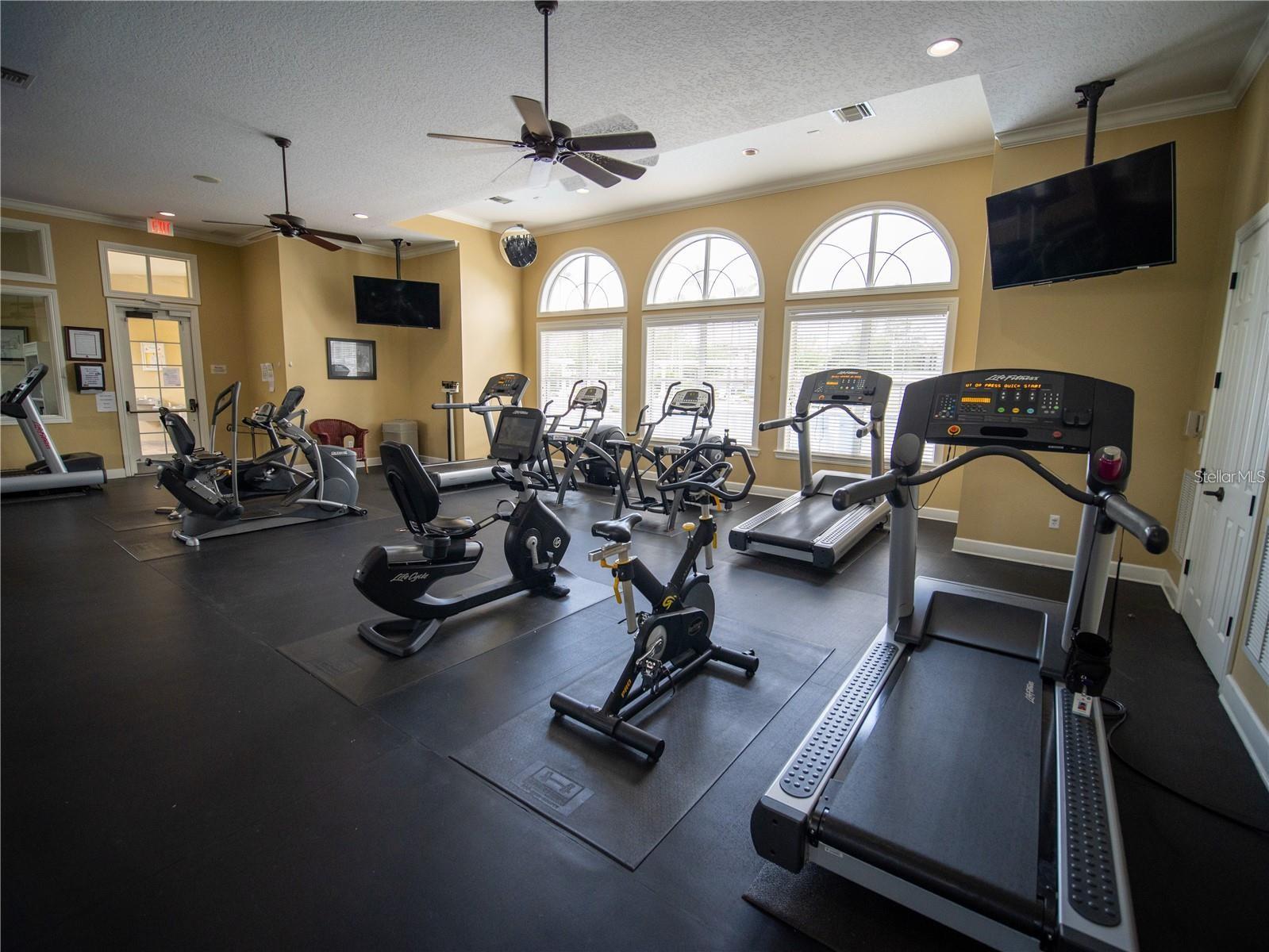 Fitness room with treadmills, bikes, and elliptical machines beneath three arched windows.