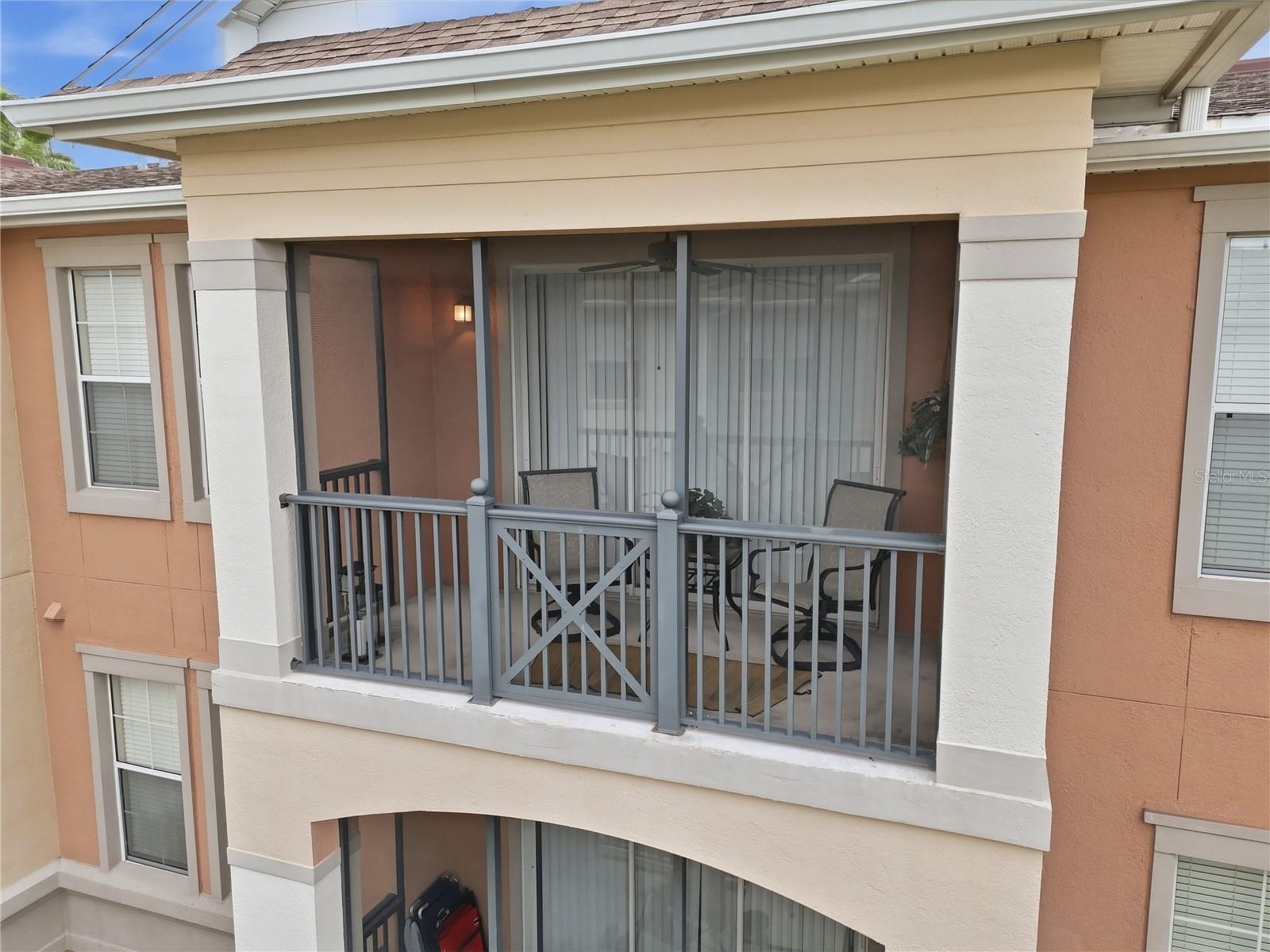 Covered condominium balcony with gray railings, sliding glass doors, and patio seating.