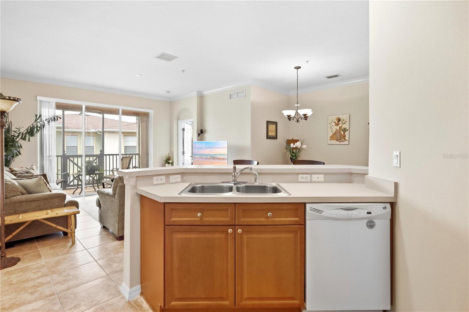 Open-plan kitchen with wood cabinets and double sink, looking toward the living area and balcony.