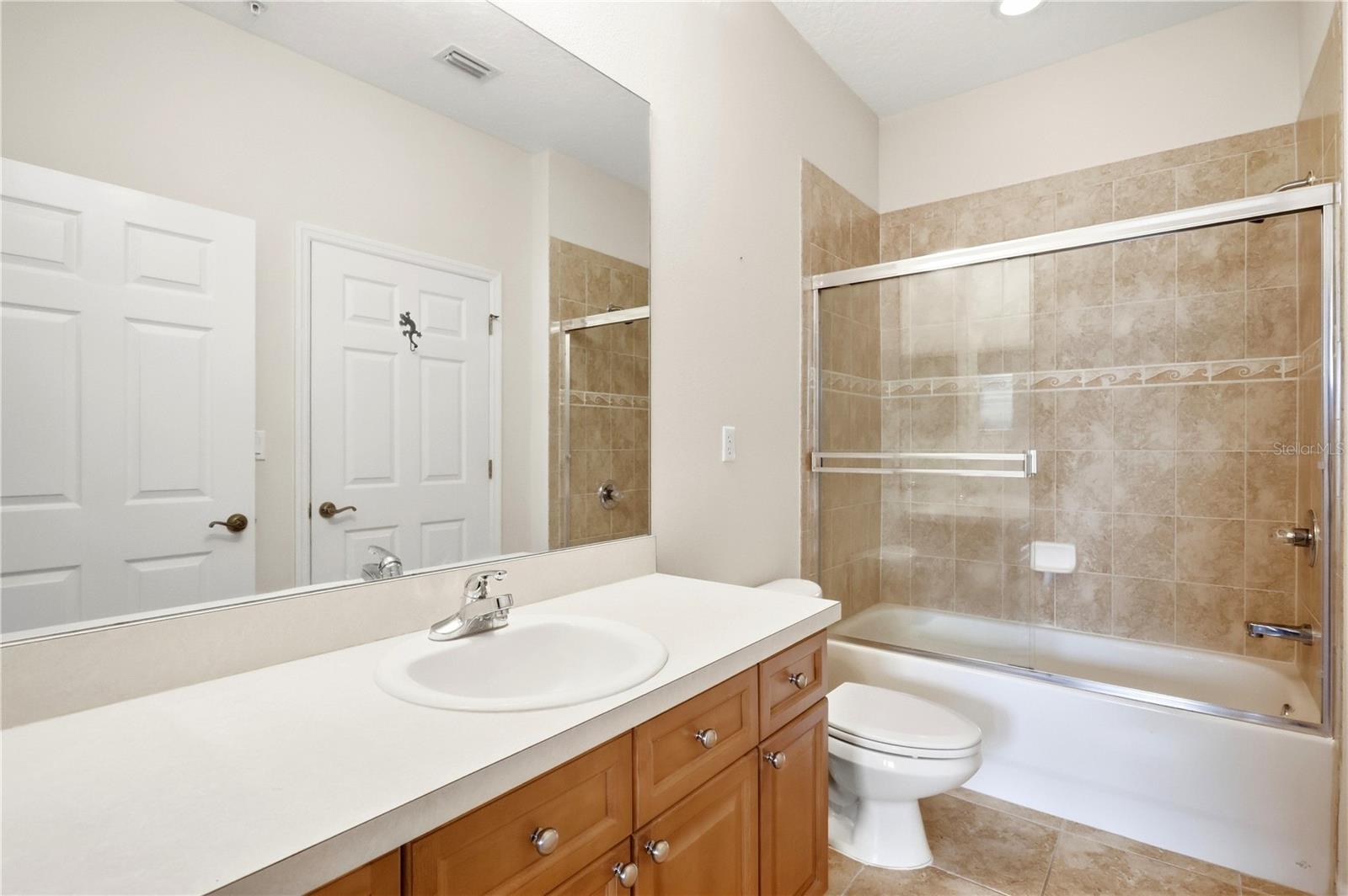 Bathroom with a long wood vanity, oval sink, and tan-tiled tub-shower enclosure.
