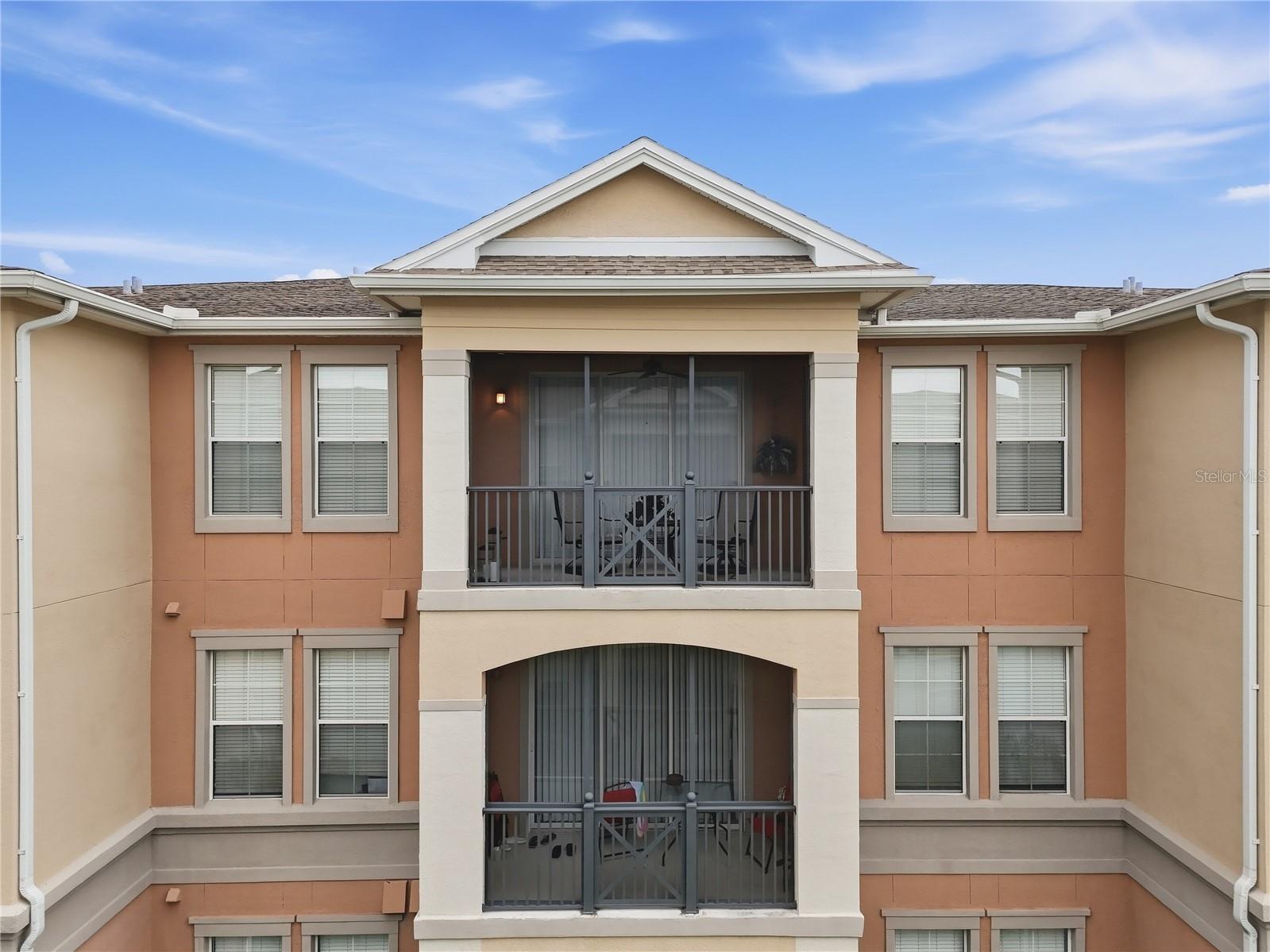 Multi-story condominium facade with peach stucco, cream trim, and stacked balconies with dark railings.