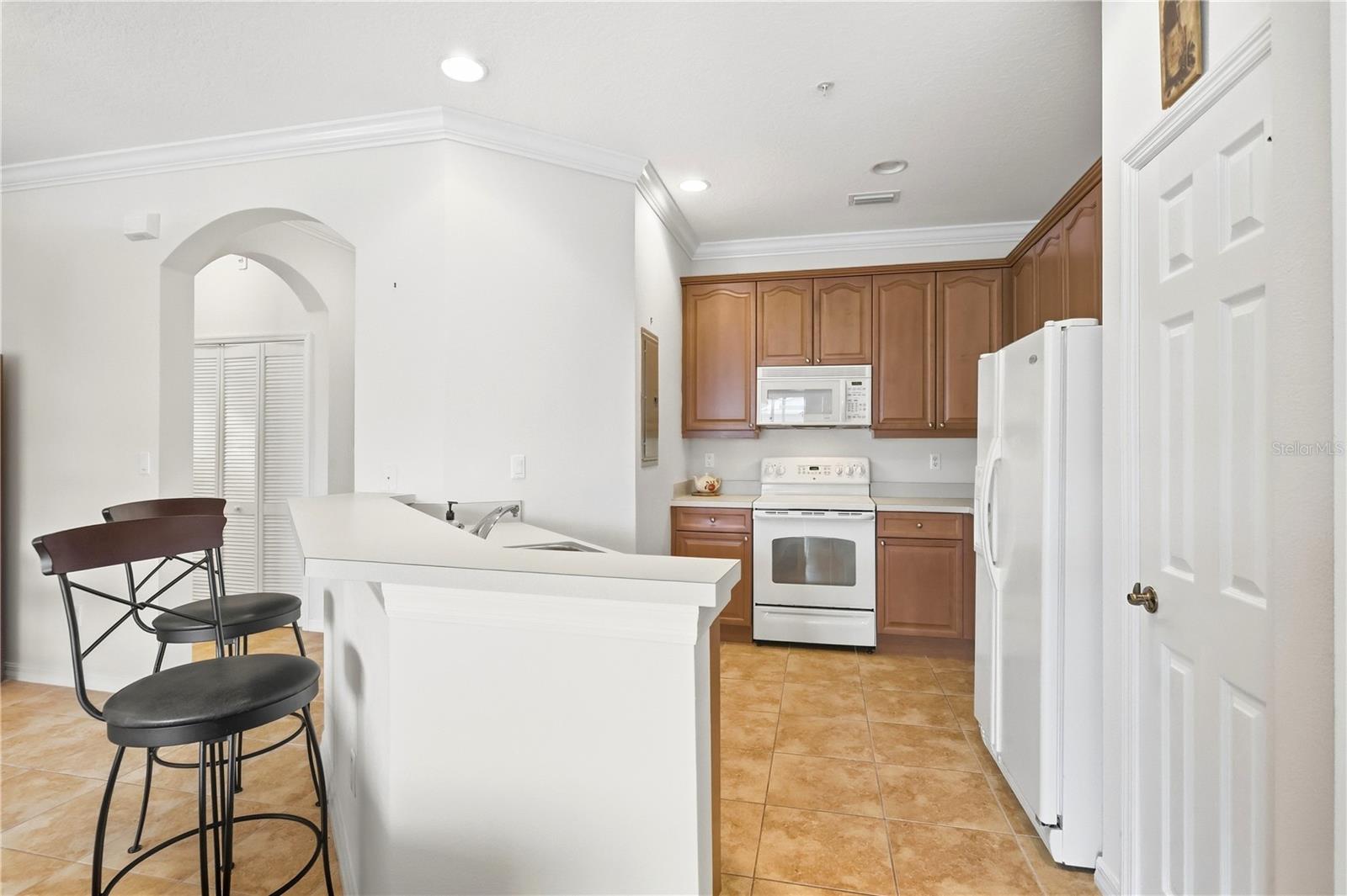 Kitchen with warm wood cabinets, white appliances, and a large breakfast bar with two stools.