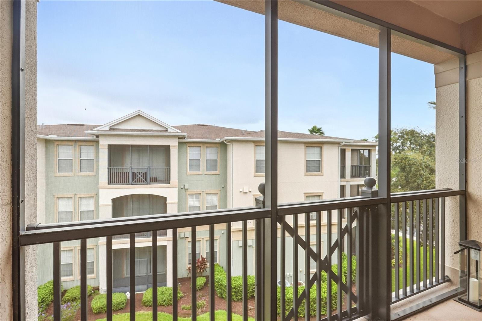 Screened balcony overlooking a neighboring apartment building and landscaped grounds.