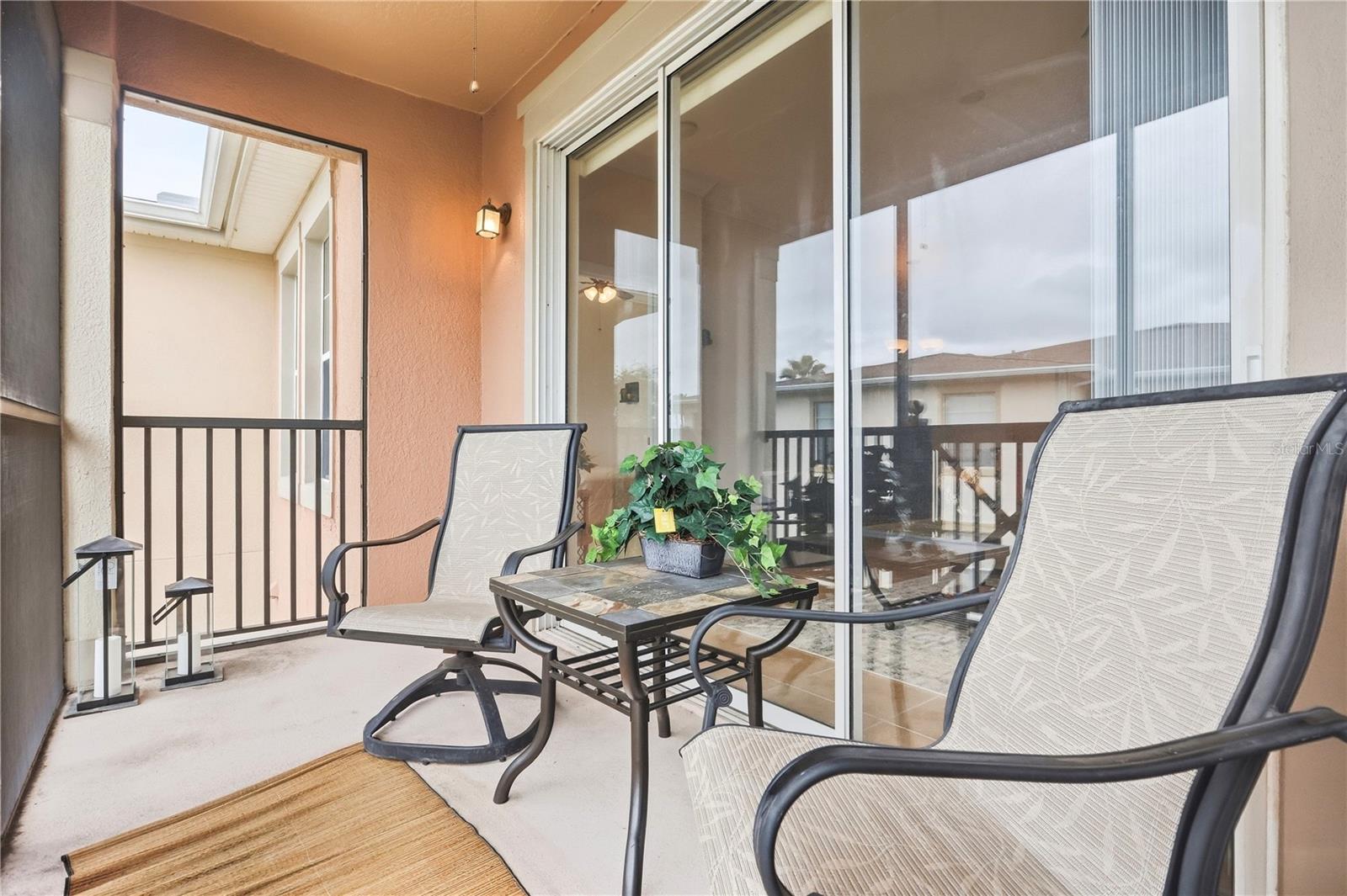Covered condo balcony with mesh chairs, a tiled patio table, and sliding glass doors.