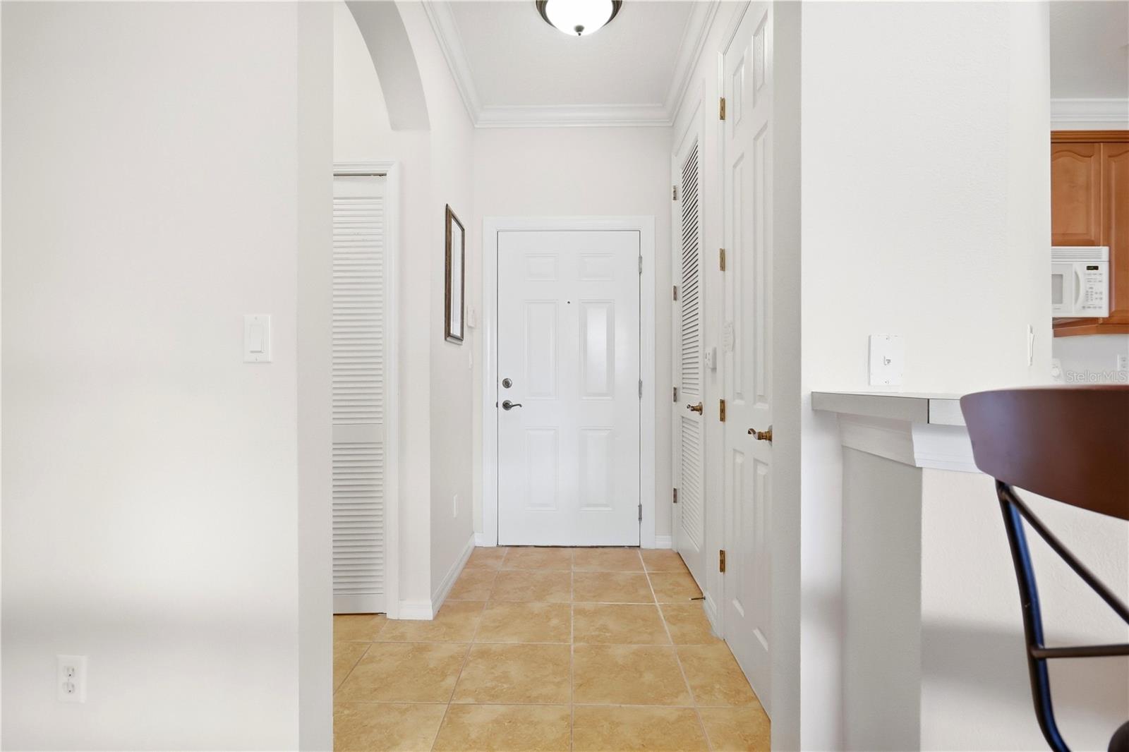 Entry hall with tan tile flooring, white doors, and a glimpse of the kitchen.