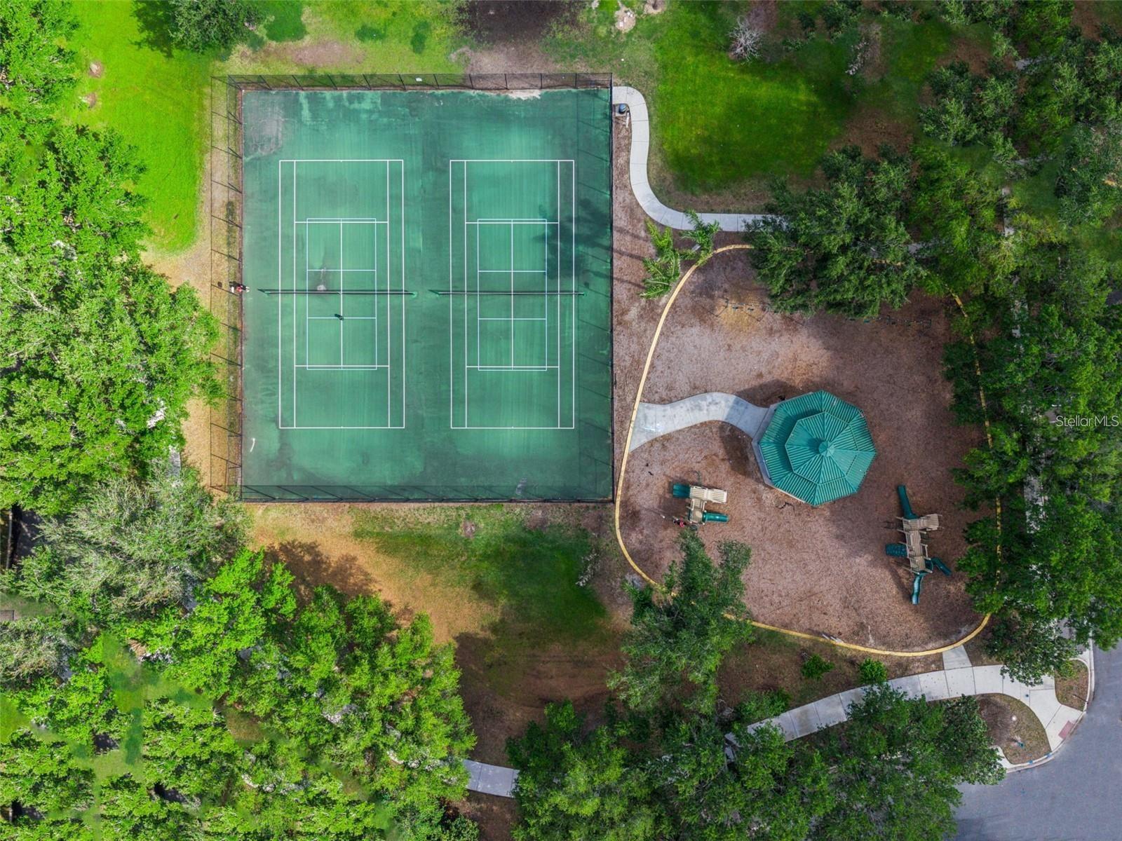Aerial view of two tennis courts beside a landscaped play area and teal gazebo.