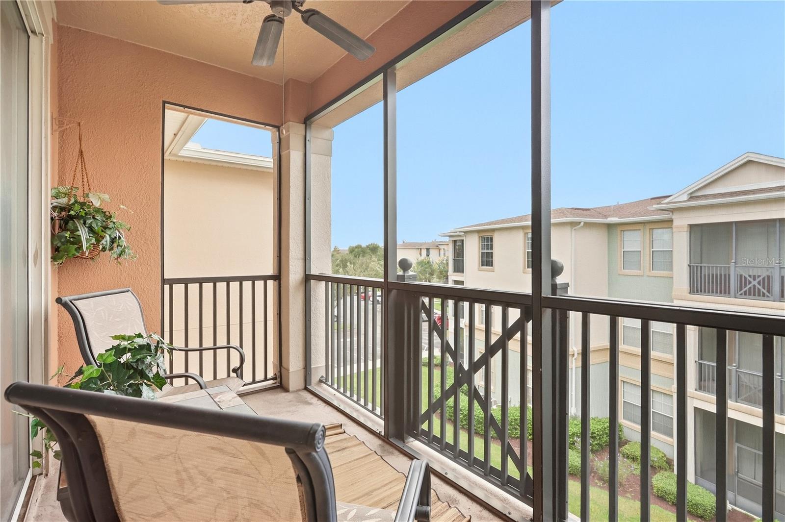 Screened balcony with seating and a hanging plant overlooking neighboring buildings.